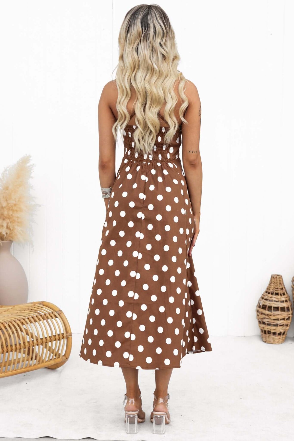 Back view of a woman wearing a brown polka dot midi dress with adjustable straps and square neckline.