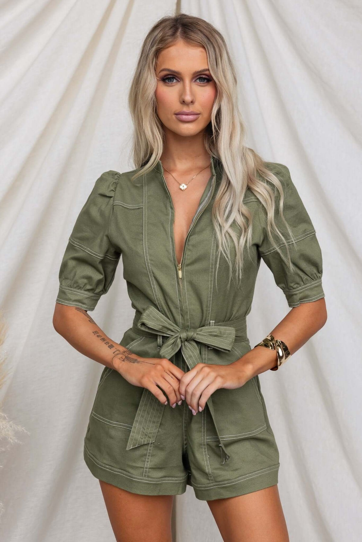 Jade denim playsuit with zip-up front, pockets, and elastic details, styled with removable belt and natural backdrop.