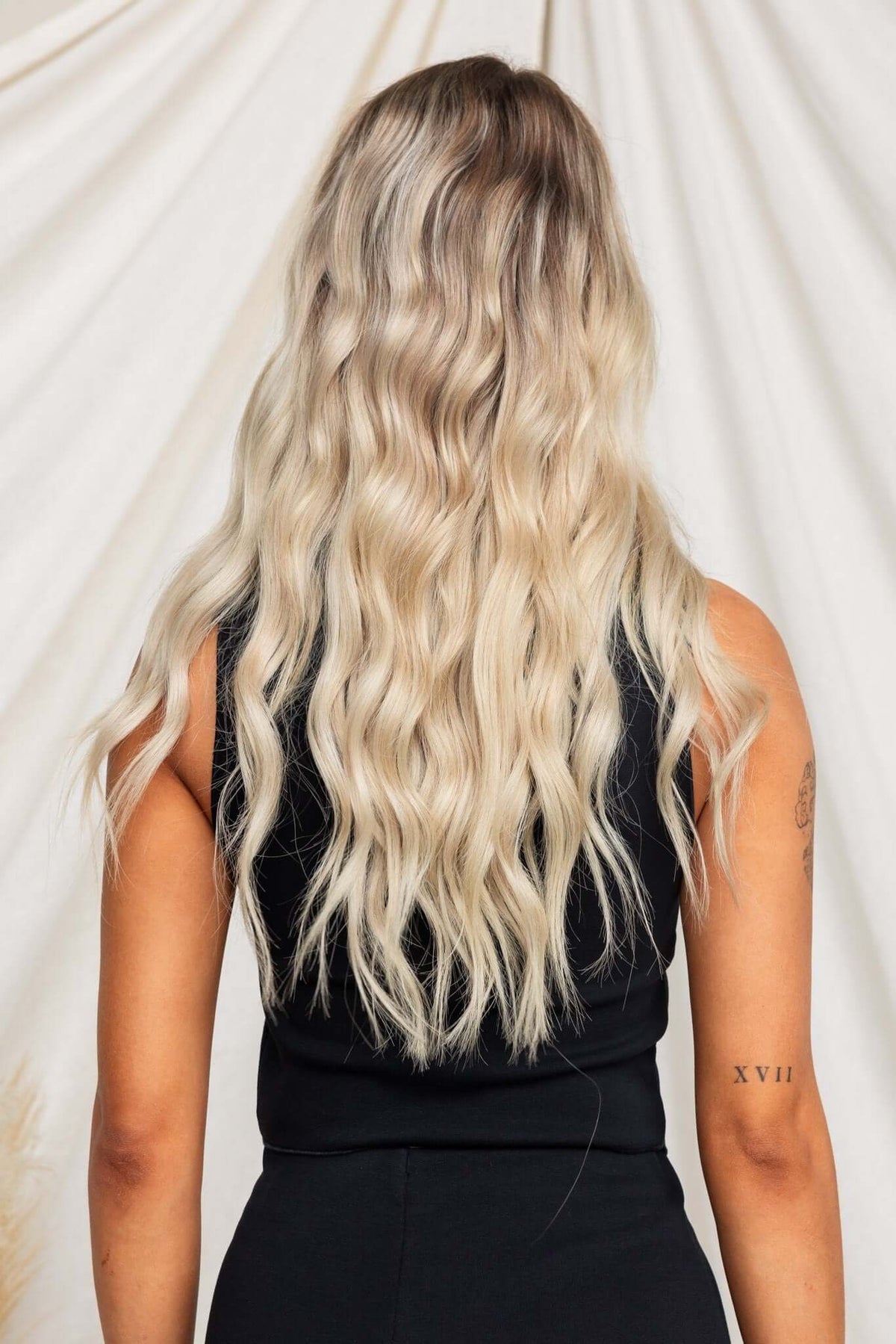 Model showcasing long, wavy blonde hair from the back while wearing a black sleeveless top.