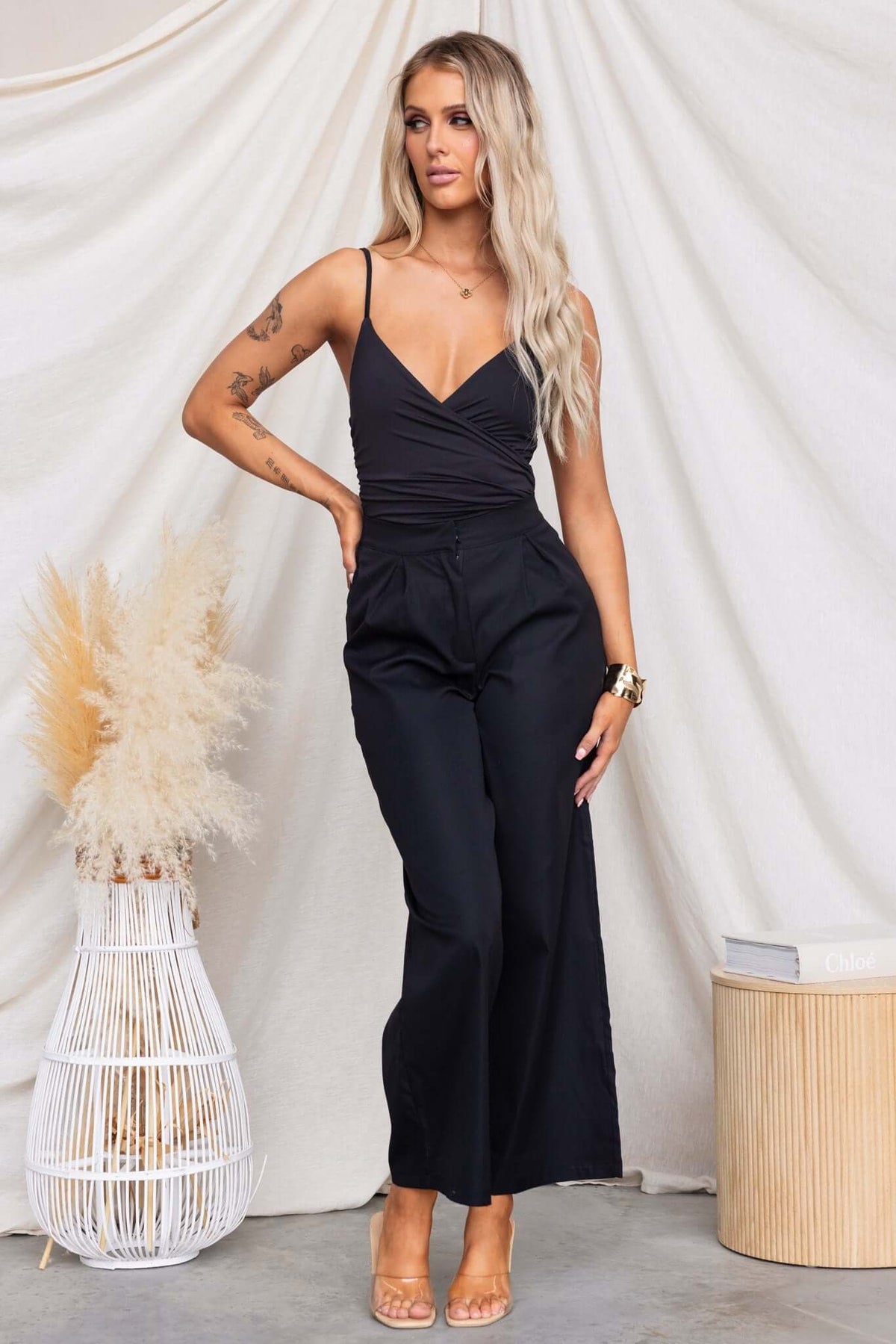 Model wearing an Oskar bodysuit with adjustable straps, V-neckline, and black wide-leg pants against a neutral backdrop.