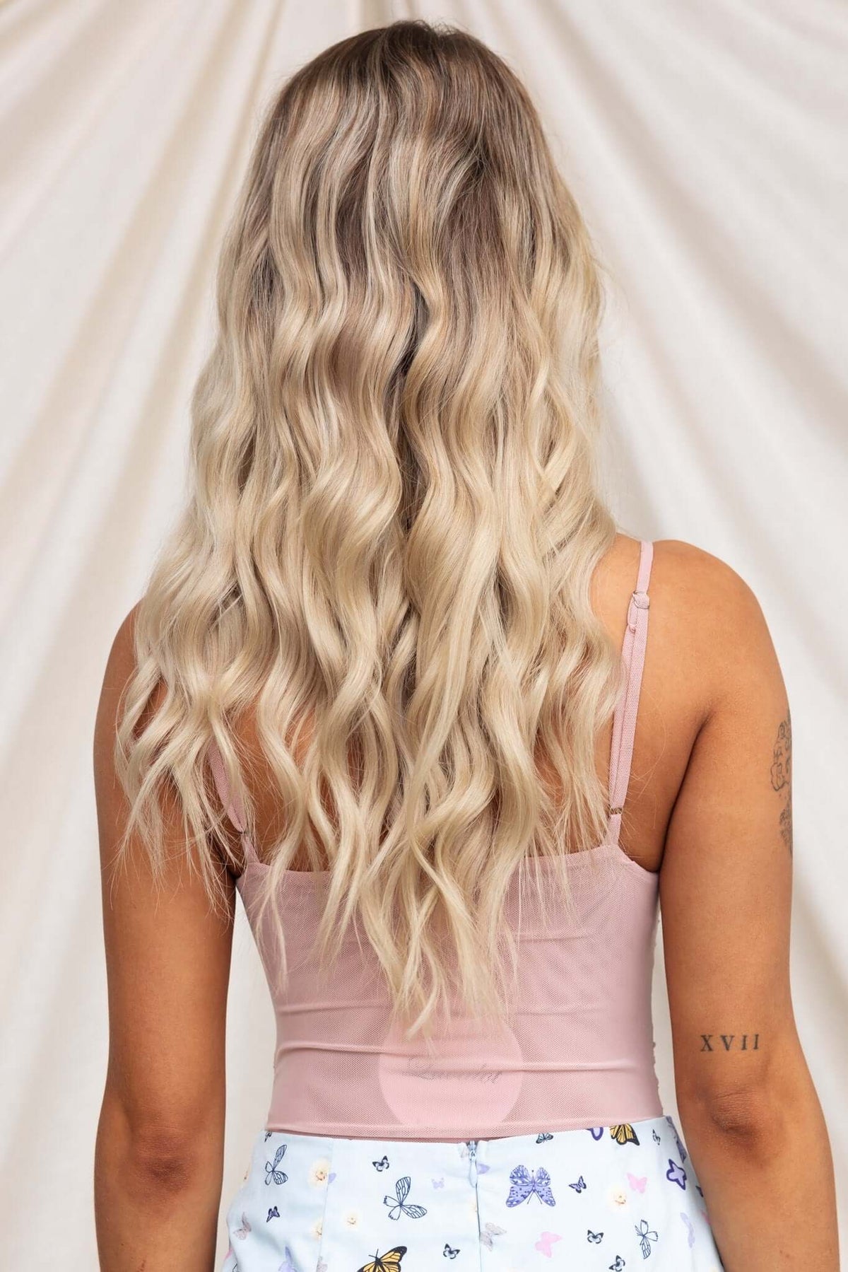Back view of a model wearing a Kiton bodysuit with adjustable straps, styled with wavy blonde hair.