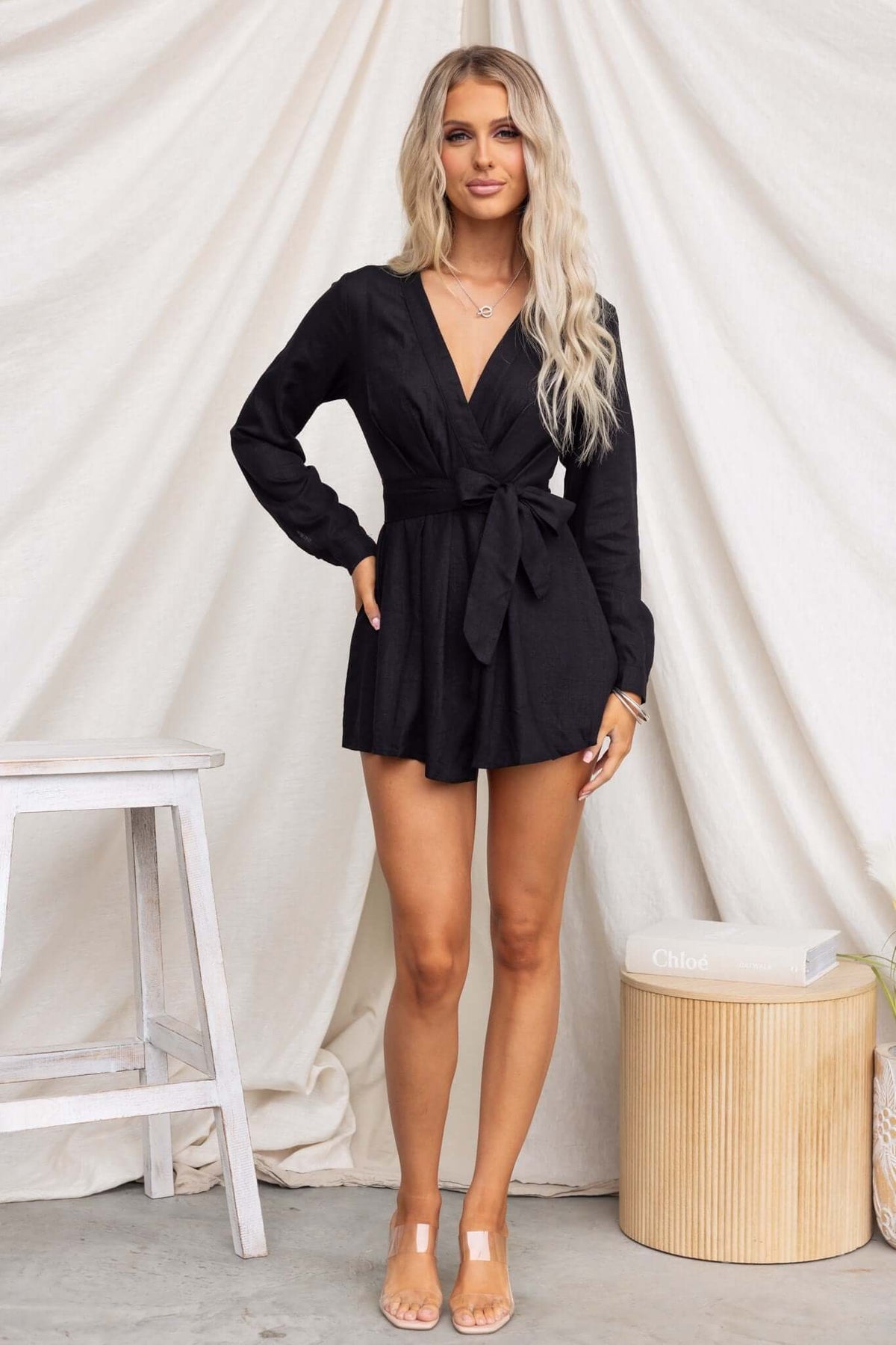 Black Hosier Playsuit with V-neckline, tie waist, and long sleeves, styled on a model against a light backdrop.