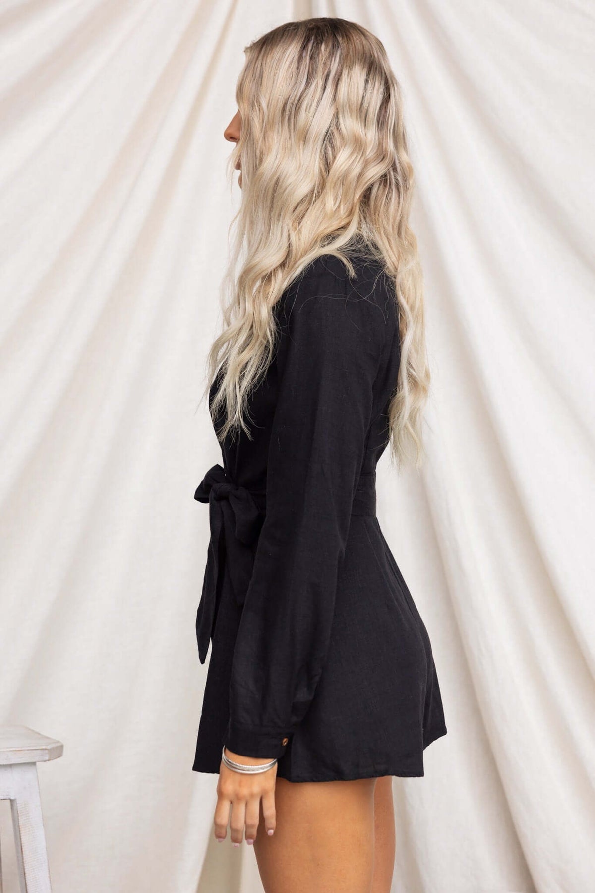 Side view of a model wearing a black Hosier playsuit with a V-neckline and removable tie.
