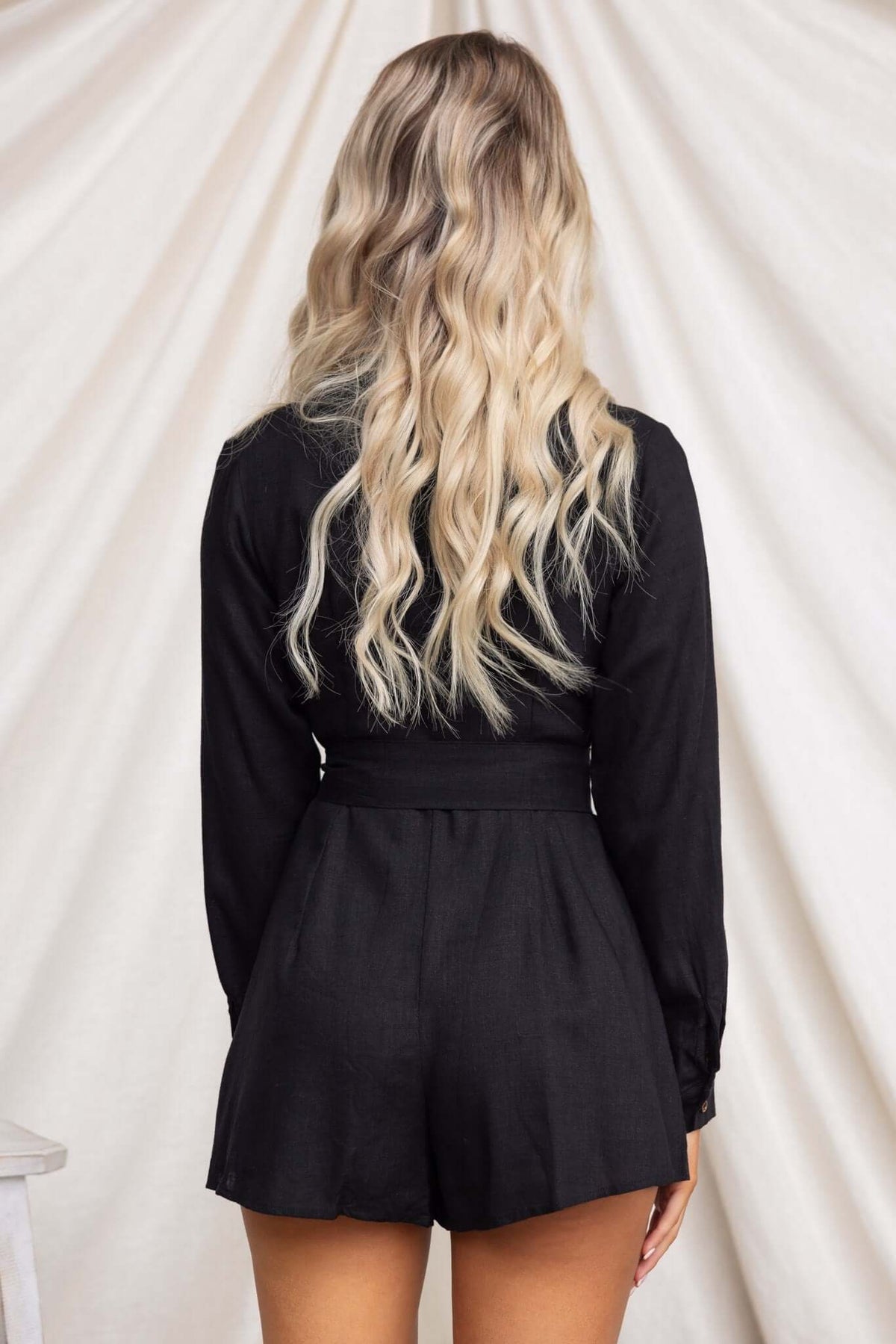 Back view of a woman wearing a black Hosier playsuit featuring long sleeves and a fitted waist.