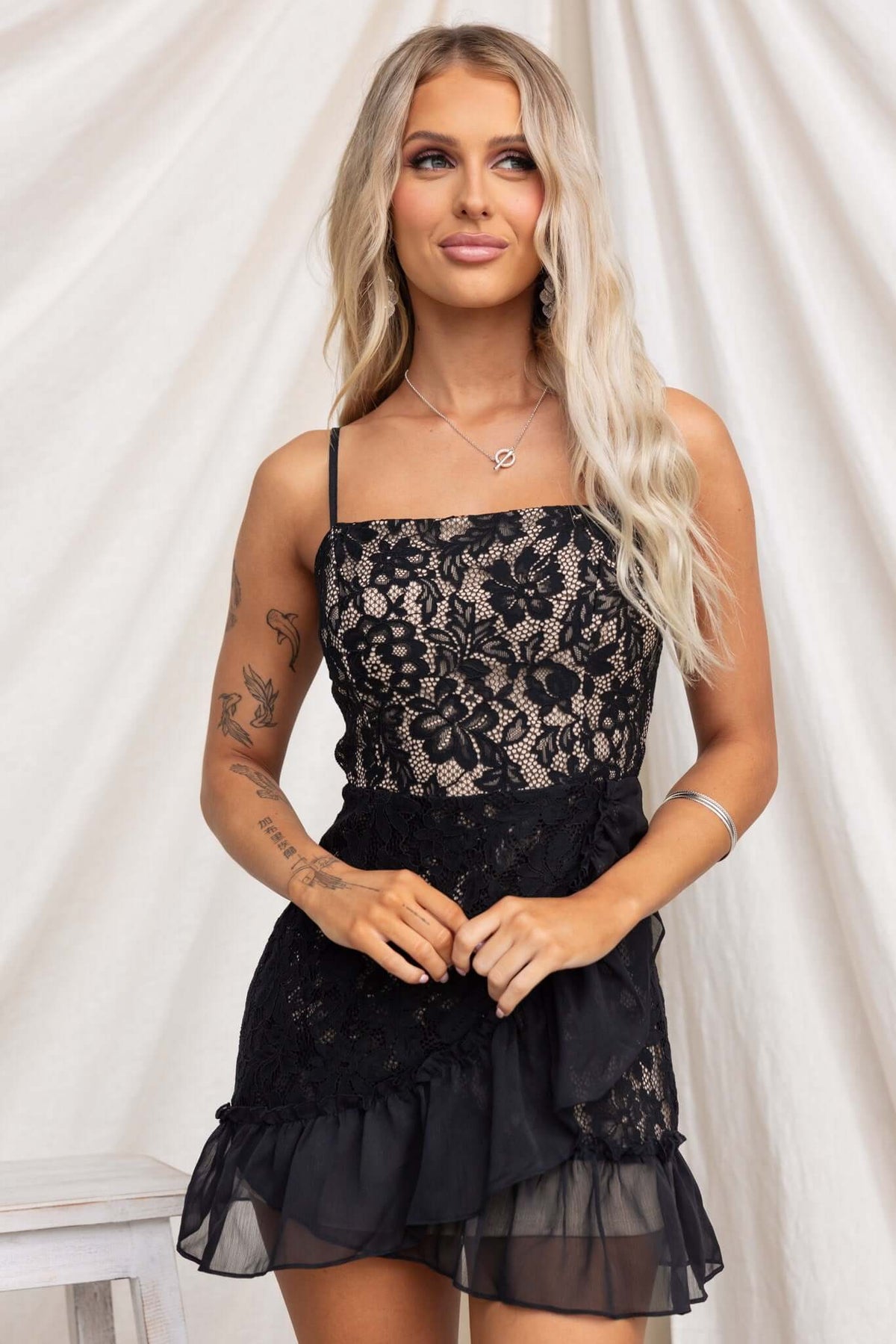 Elie Dress featuring adjustable straps, lace material, and layered ruffle hem, modeled by a woman with long blonde hair.