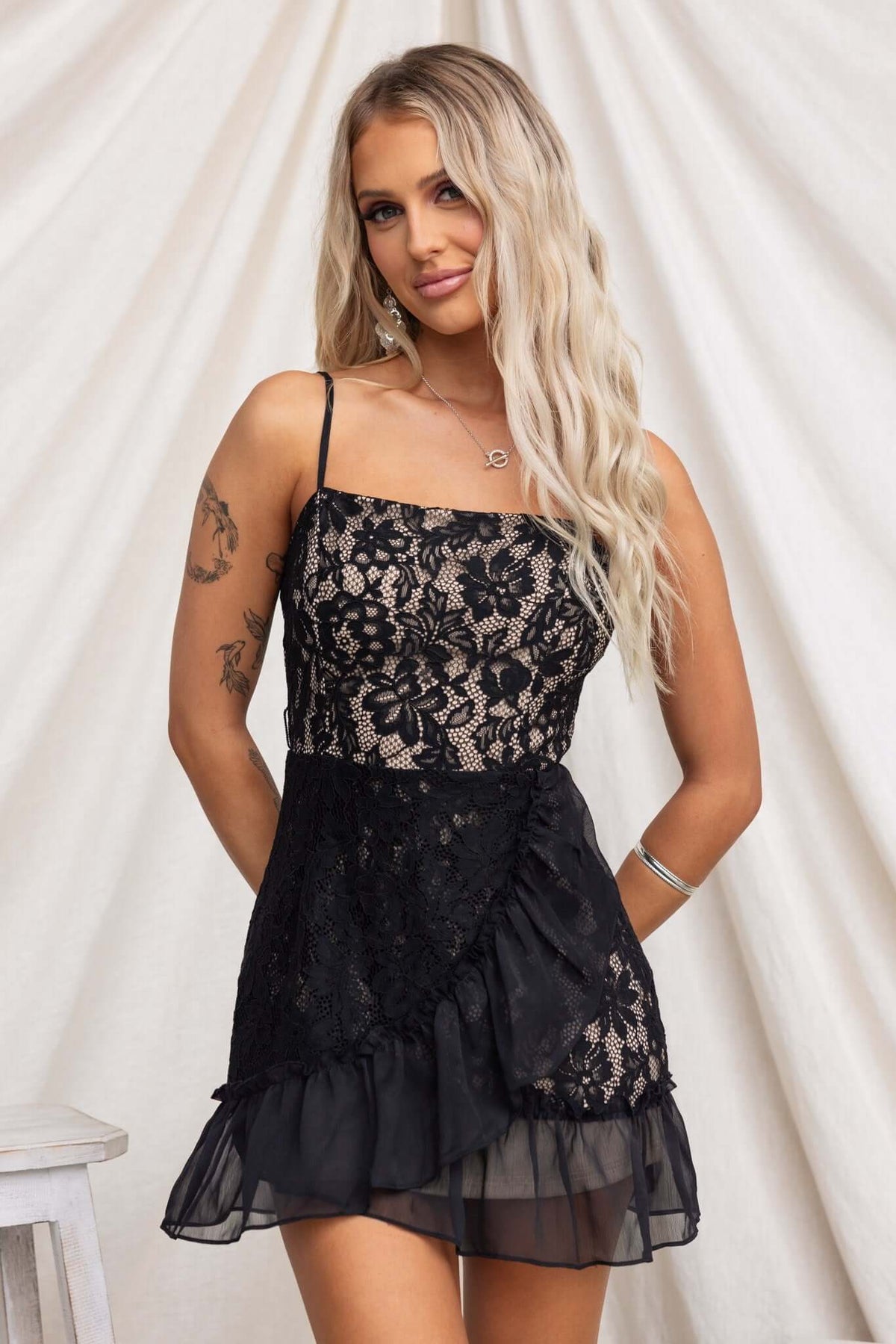 Elie Dress featuring adjustable straps and lace material, styled with a ruffled hem on a model, perfect for casual occasions.