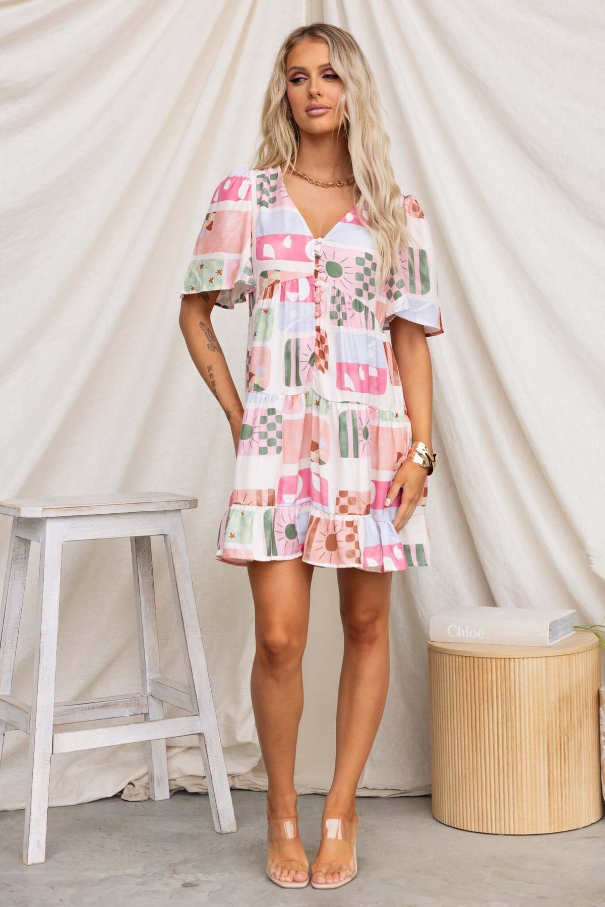 Model wearing pink Mariella dress with floral patterns, button-up front, and pockets, against a neutral backdrop.