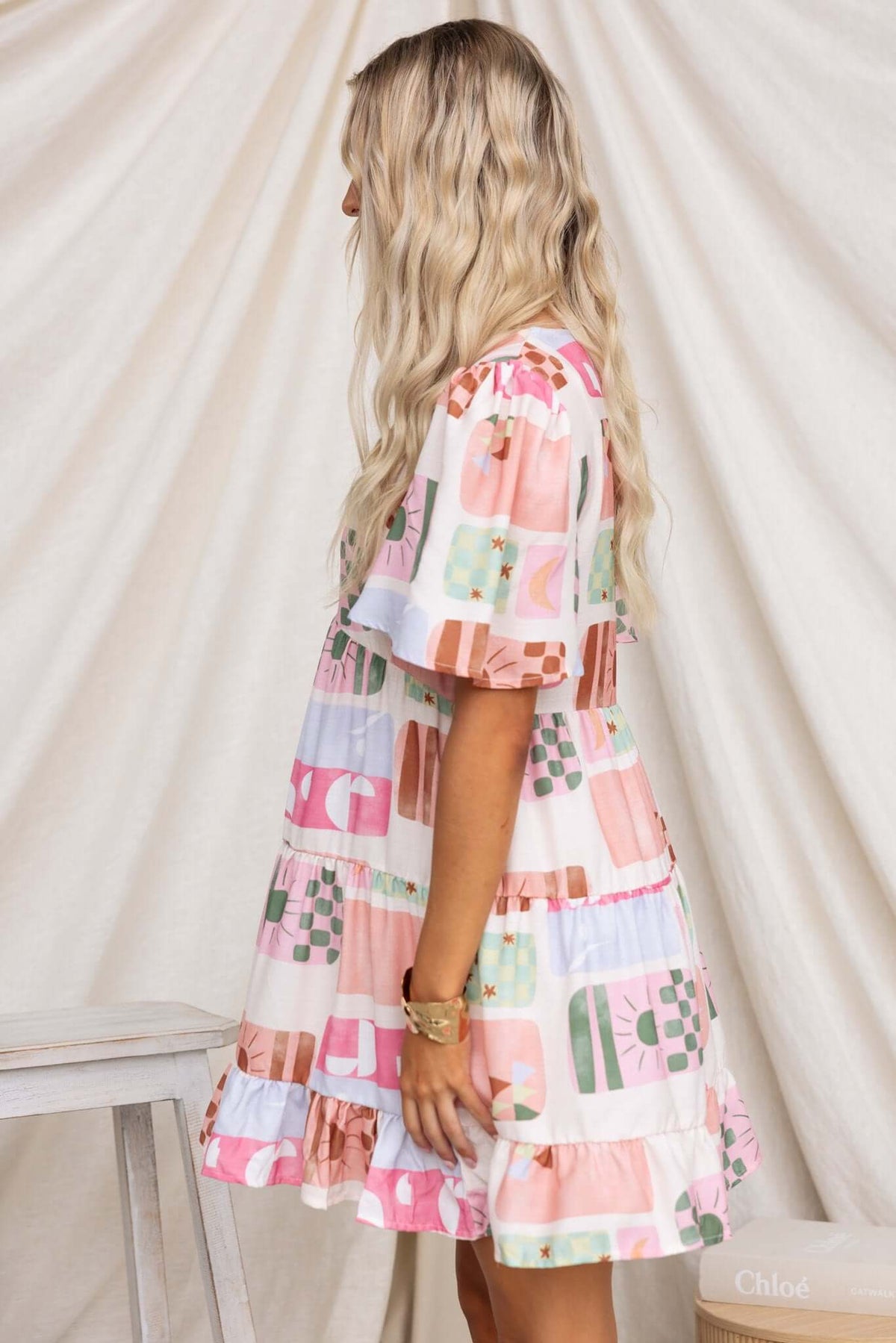 Side view of a model wearing the Mariella Dress, a colorful button-up dress with pockets and a ruffled hem.