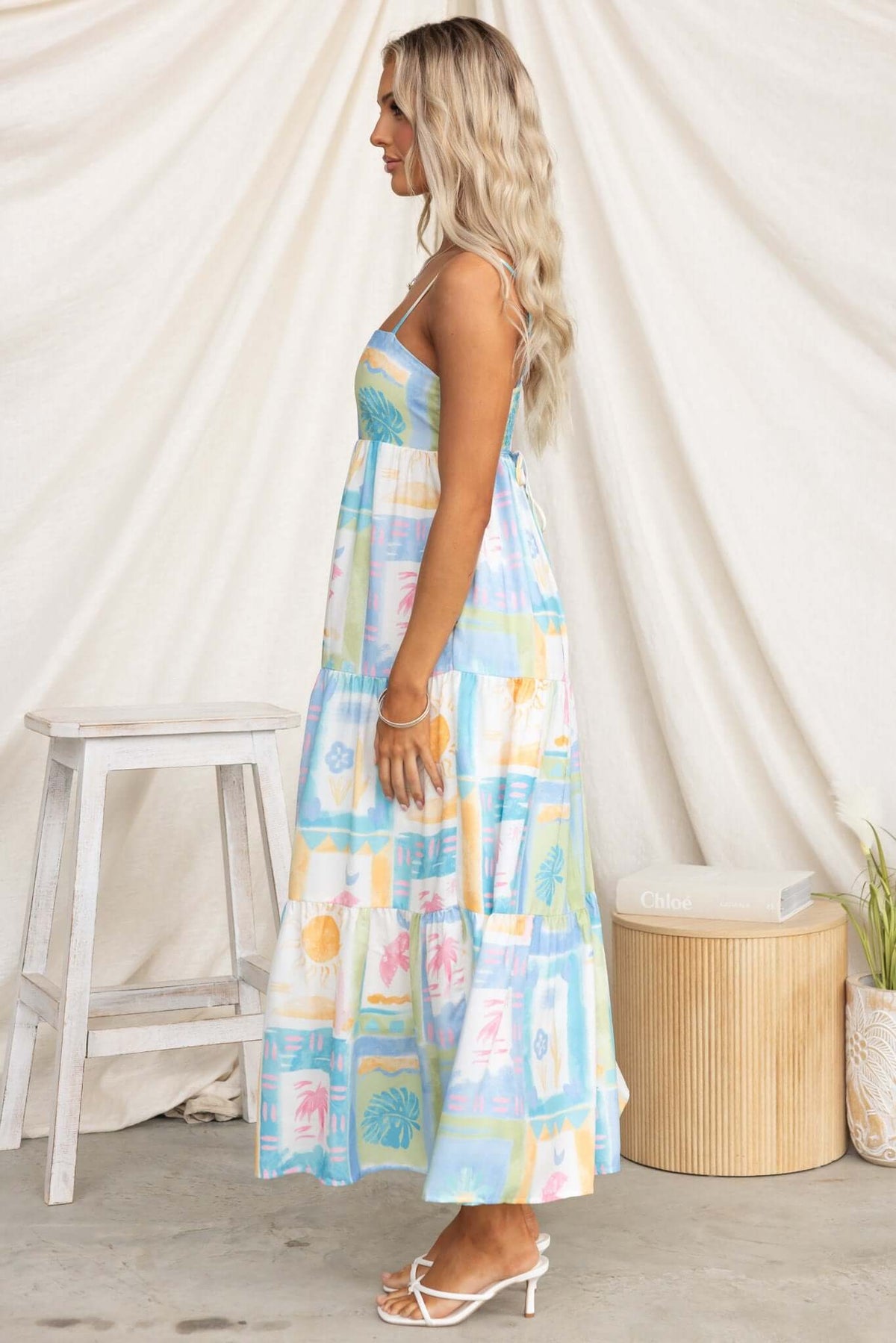 Side view of a woman in a colorful maxi dress with adjustable straps, pockets, and a relaxed fit, styled with sandals.