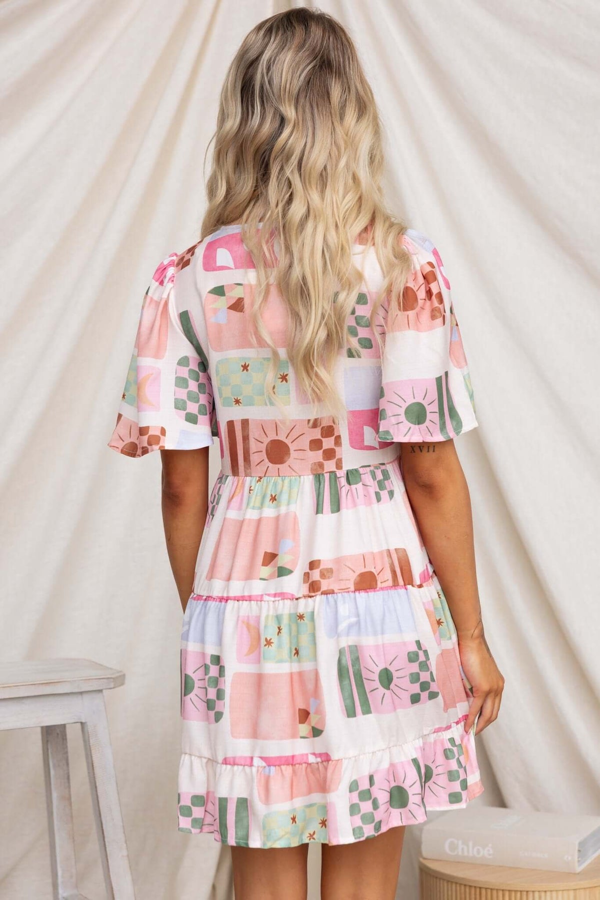 Back view of the Mariella Dress featuring a colorful patchwork design and flutter sleeves.