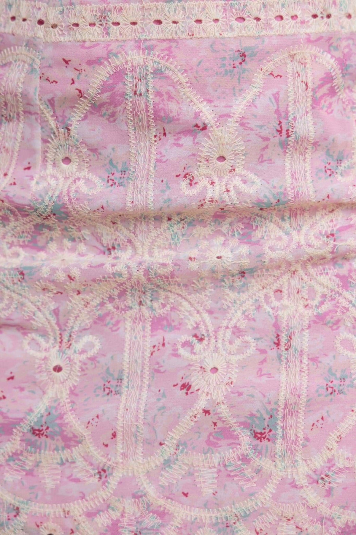 Close-up of intricate pink floral fabric with decorative lace details, perfect for crafting or fashion design projects.