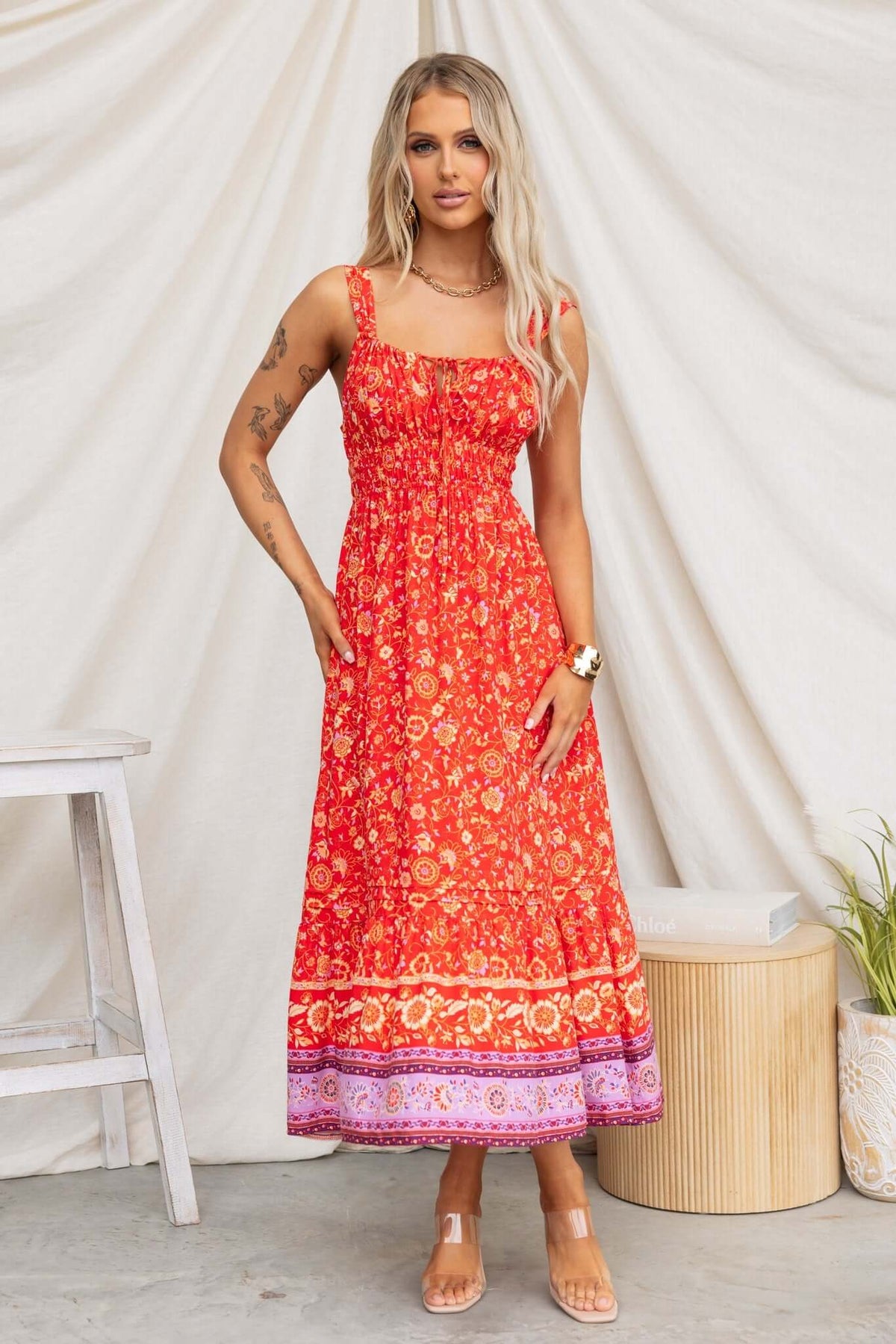 Model wearing a vibrant red Skipper Midi Dress with adjustable straps and floral print against a neutral background.
