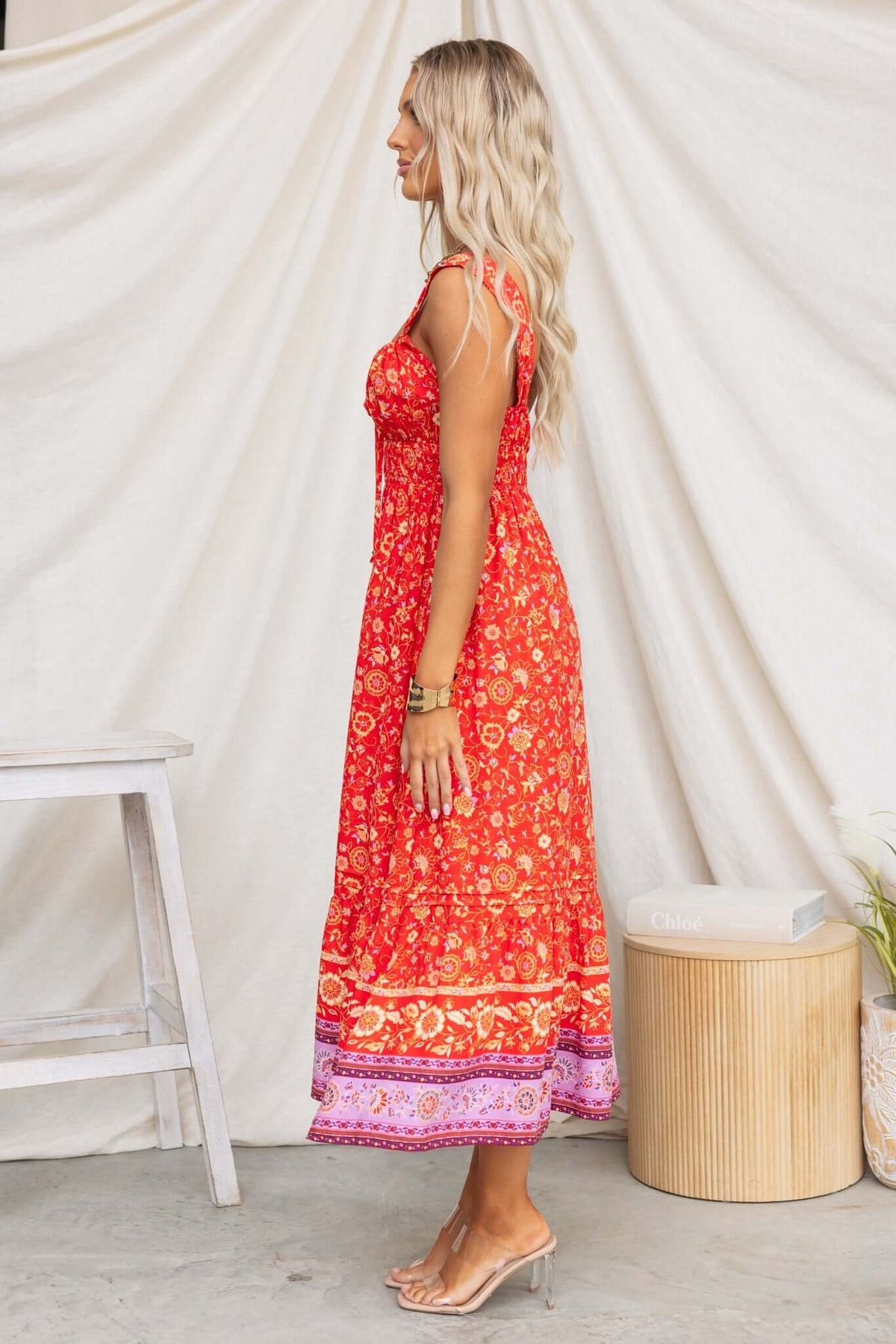 Model in a side view wearing a bright red Skipper Midi Dress with floral print and adjustable straps.