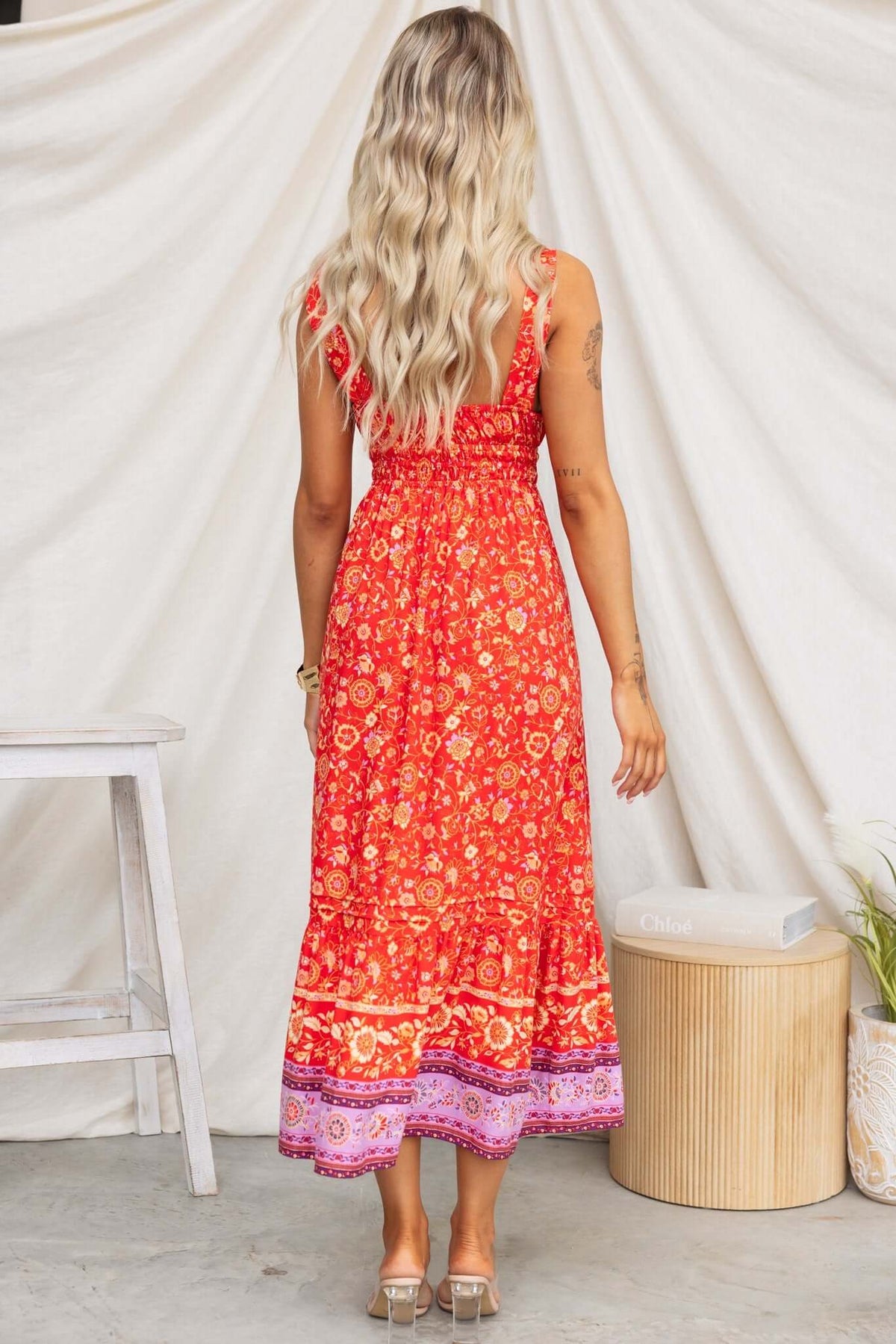 Model wearing a vibrant red Skipper Midi Dress with floral patterns, showcasing adjustable straps and a cinched waist.