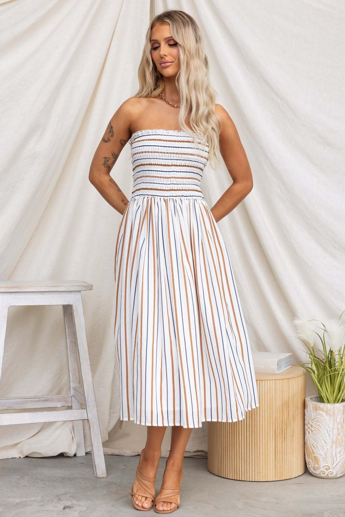 Model wearing Elkie Midi Dress, a strapless cotton dress with vertical stripes, styled with tan sandals.