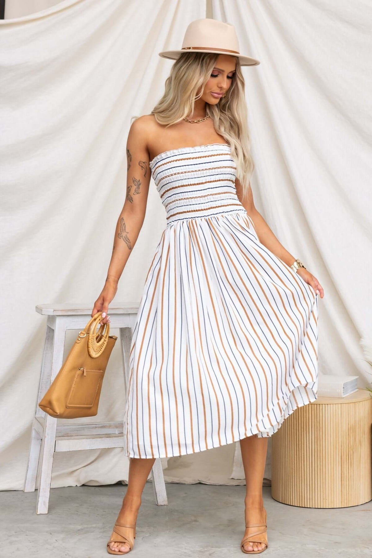 Model wearing Elkie Midi Dress, strapless with elastic bodice and striped design, paired with a hat and bag.