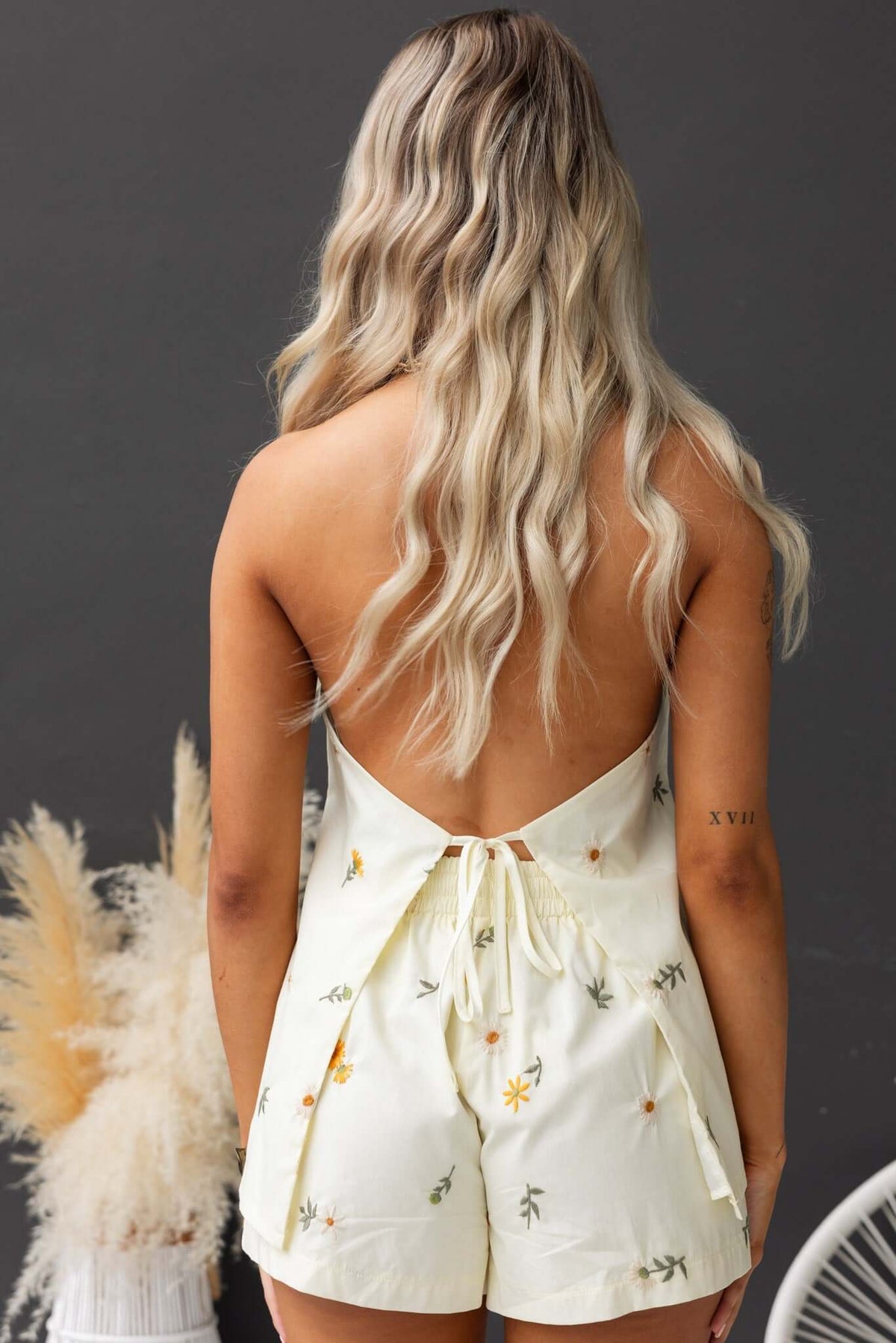 Back view of a model wearing the Tori Top, featuring a tie neckline and floral embroidery on a light yellow fabric.