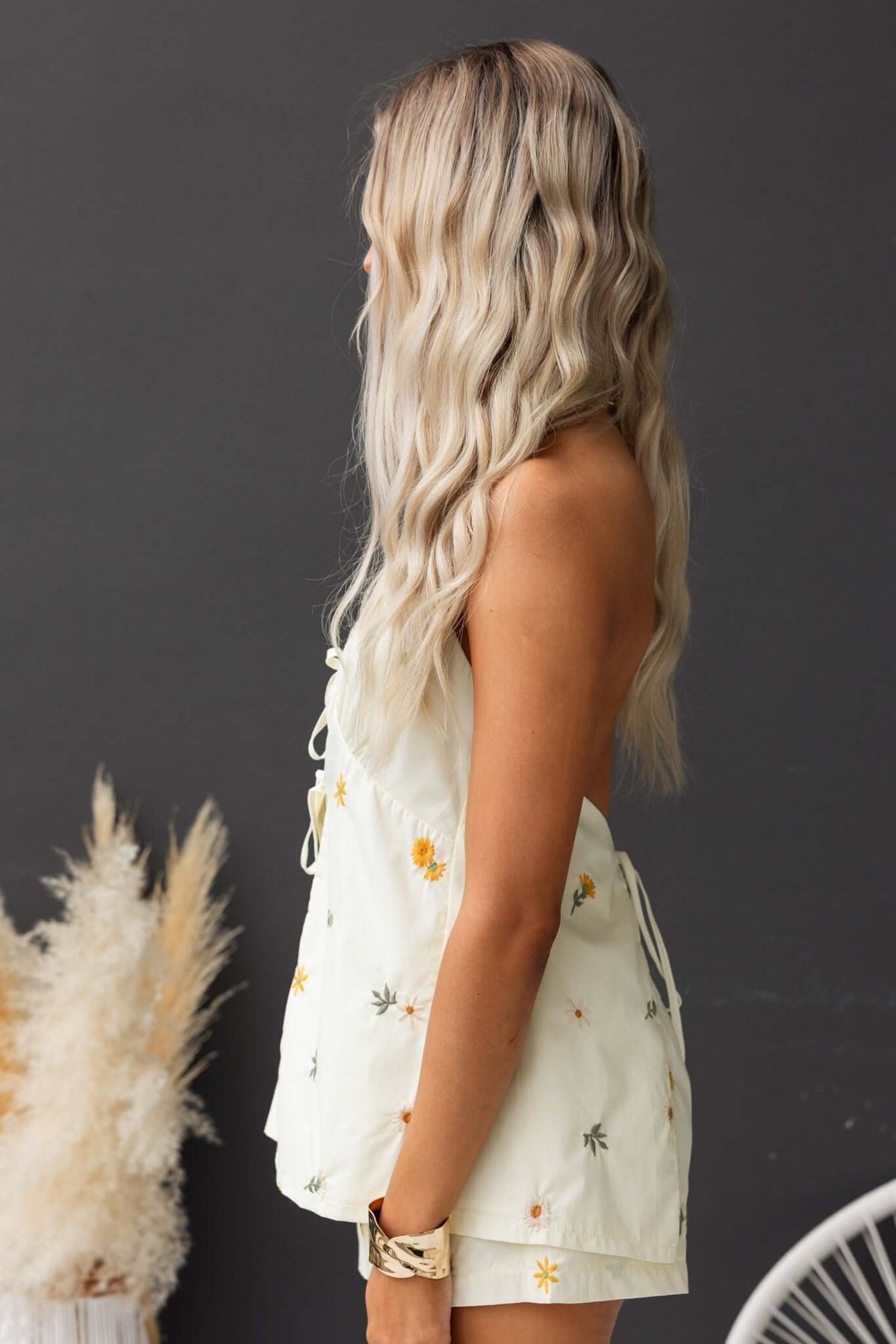 Side view of Tori Top, a light cotton top with tie neckline and floral embroidery, worn by a model with long wavy hair.