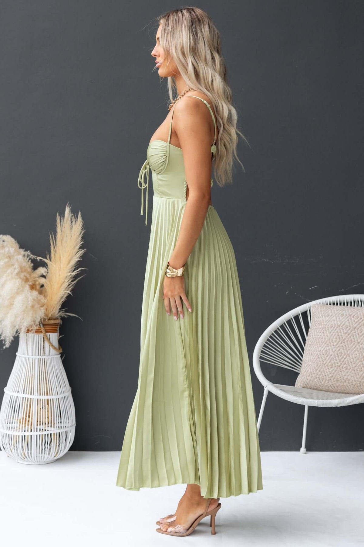Side view of a model in a green Danette Maxi Dress with adjustable straps and pleated skirt, showcasing elegant style.