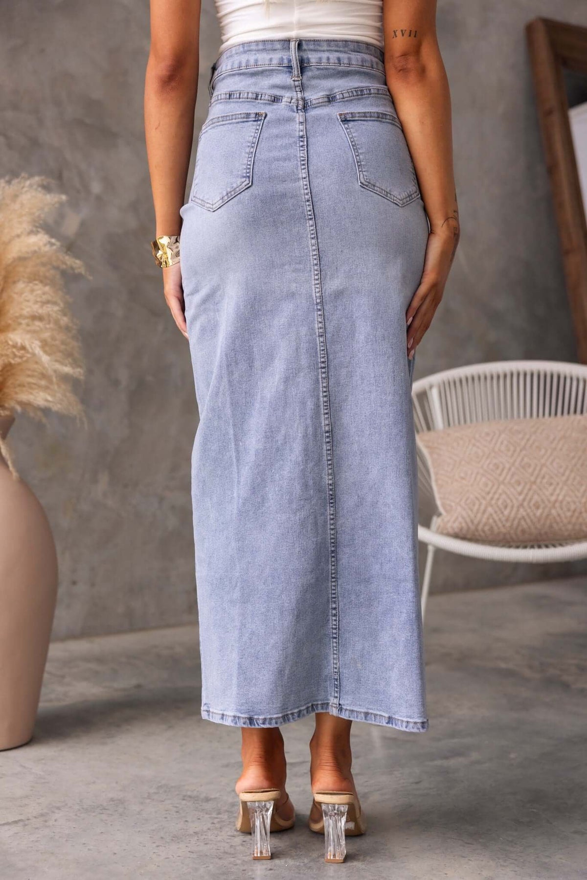 Back view of Naomi Denim Maxi Skirt in light blue, featuring mid-high waist, pockets, and a front split, styled with a white top.