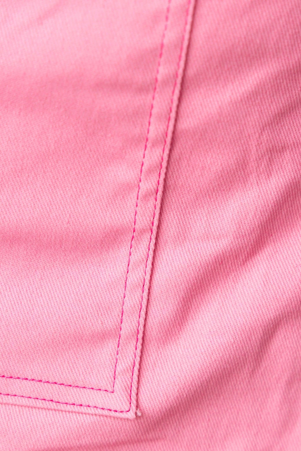 Close-up of pink denim fabric showcasing clean stitching and texture, ideal for stylish summer wear.