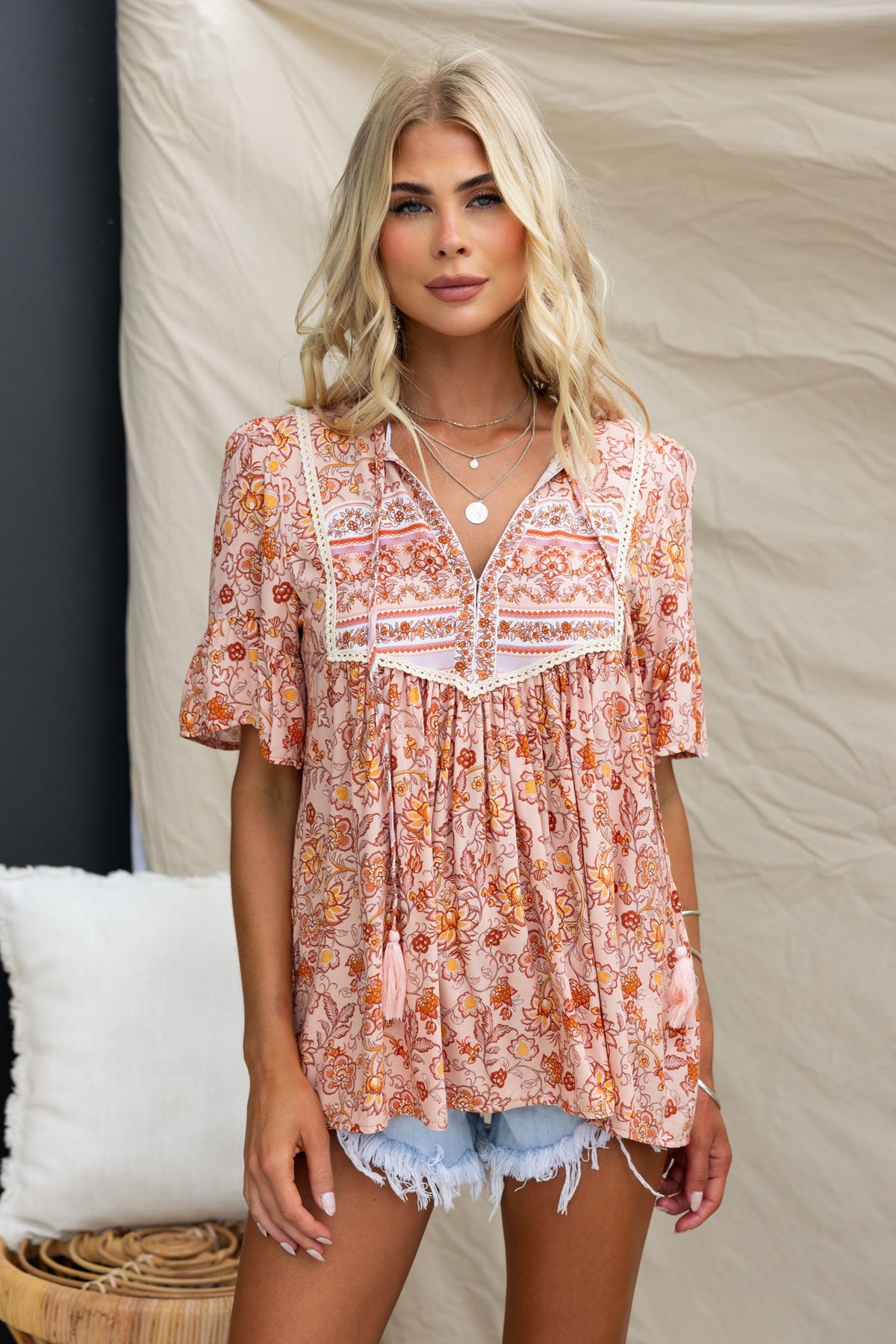 Floral print Kyra Top with V-neckline and tie detail, styled with denim shorts for a relaxed summer look.