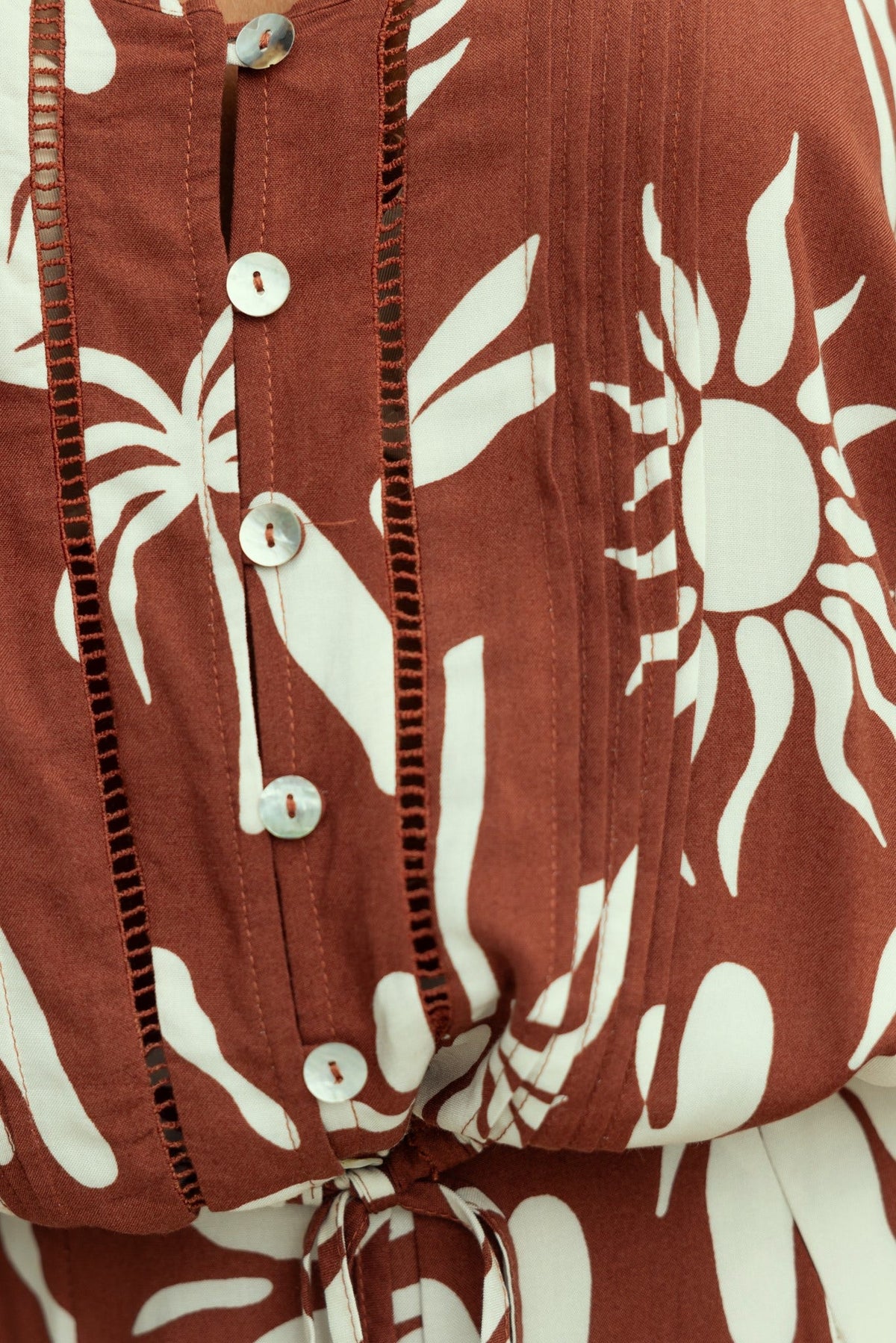 Close-up of rust-colored fabric featuring bold white abstract sun designs and buttons.
