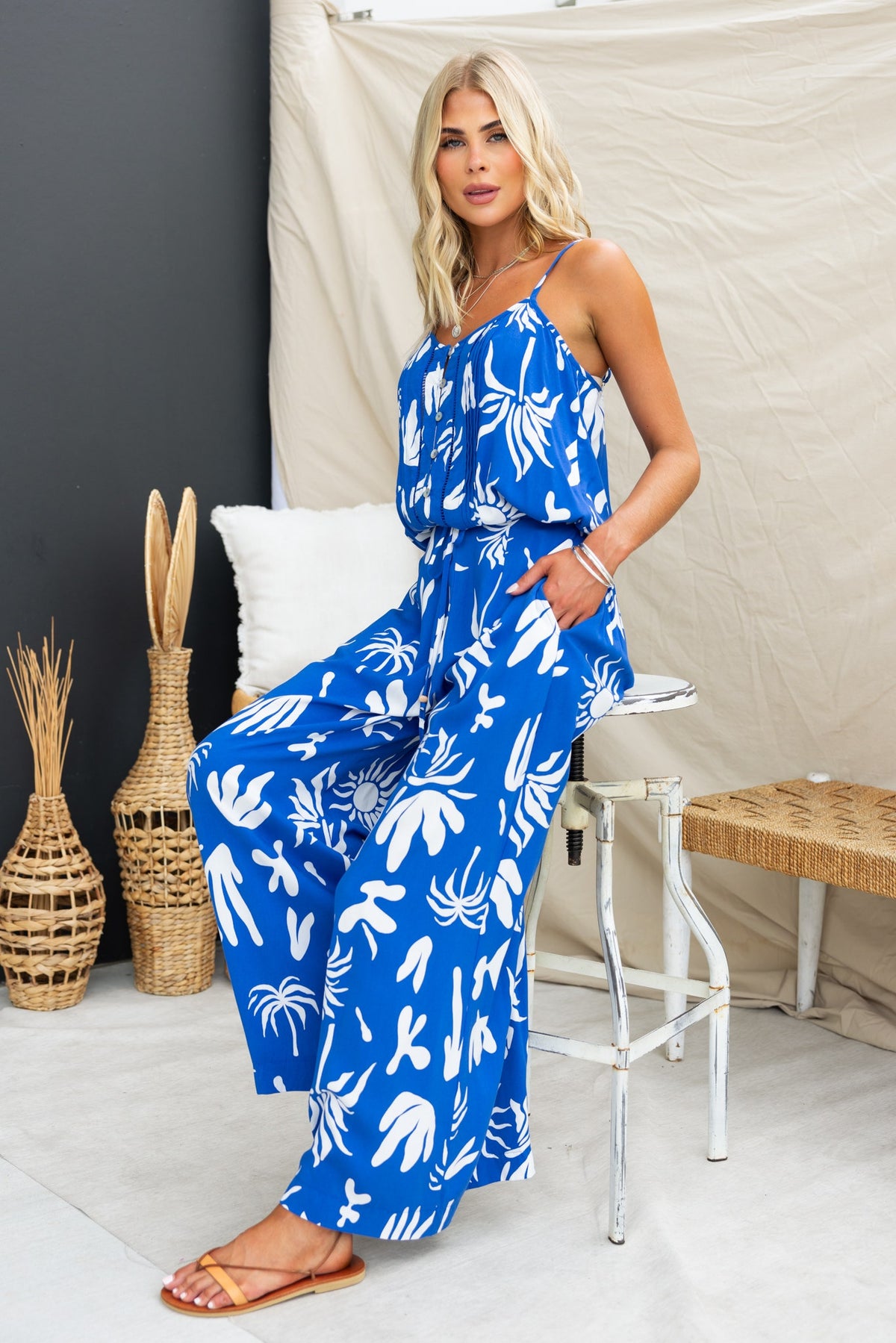 Model wearing vibrant blue abstract print jumpsuit with spaghetti straps, showcasing a stylish summer look.