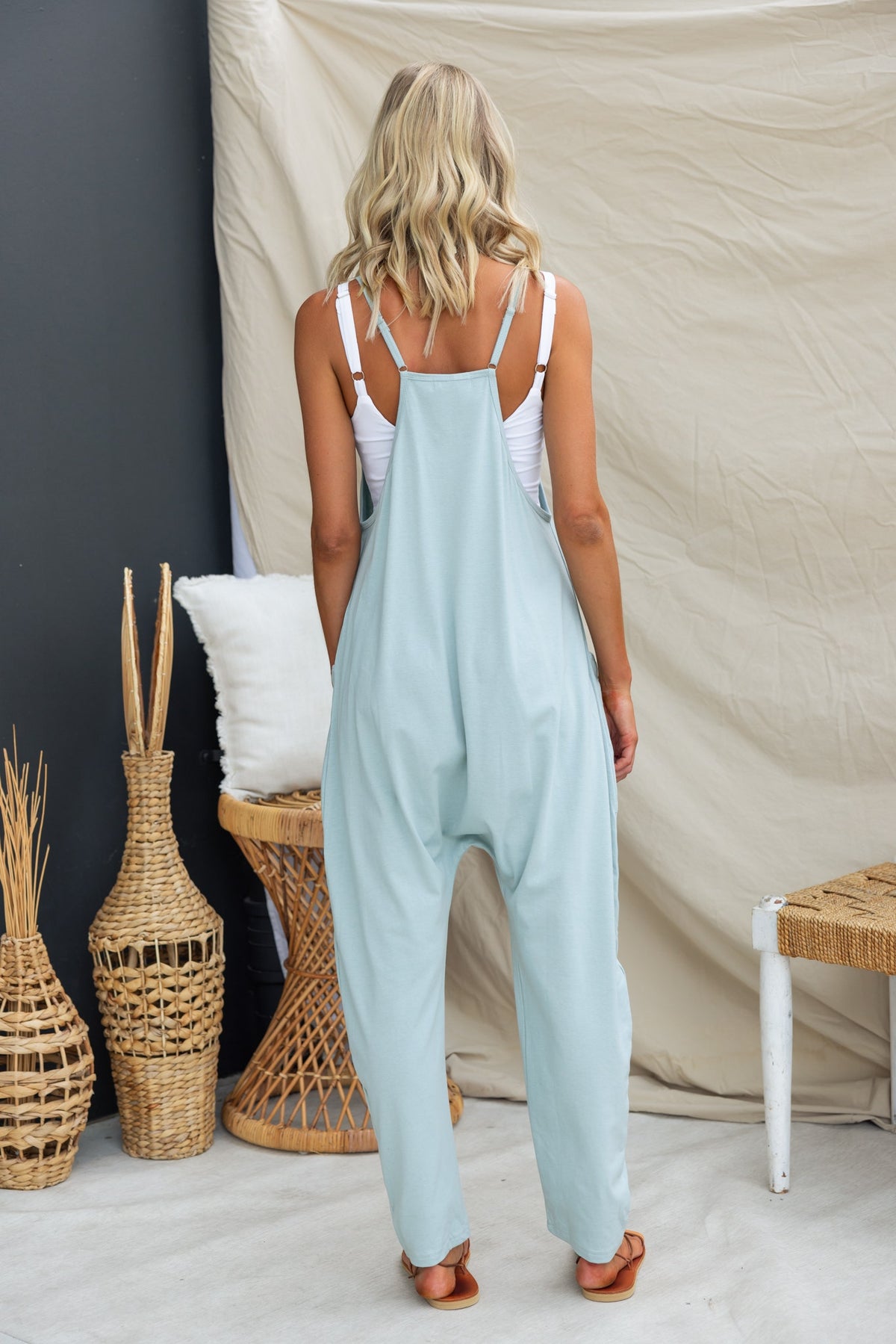 Back view of a model in a light blue Essie jumpsuit with adjustable straps and drop crotch style.