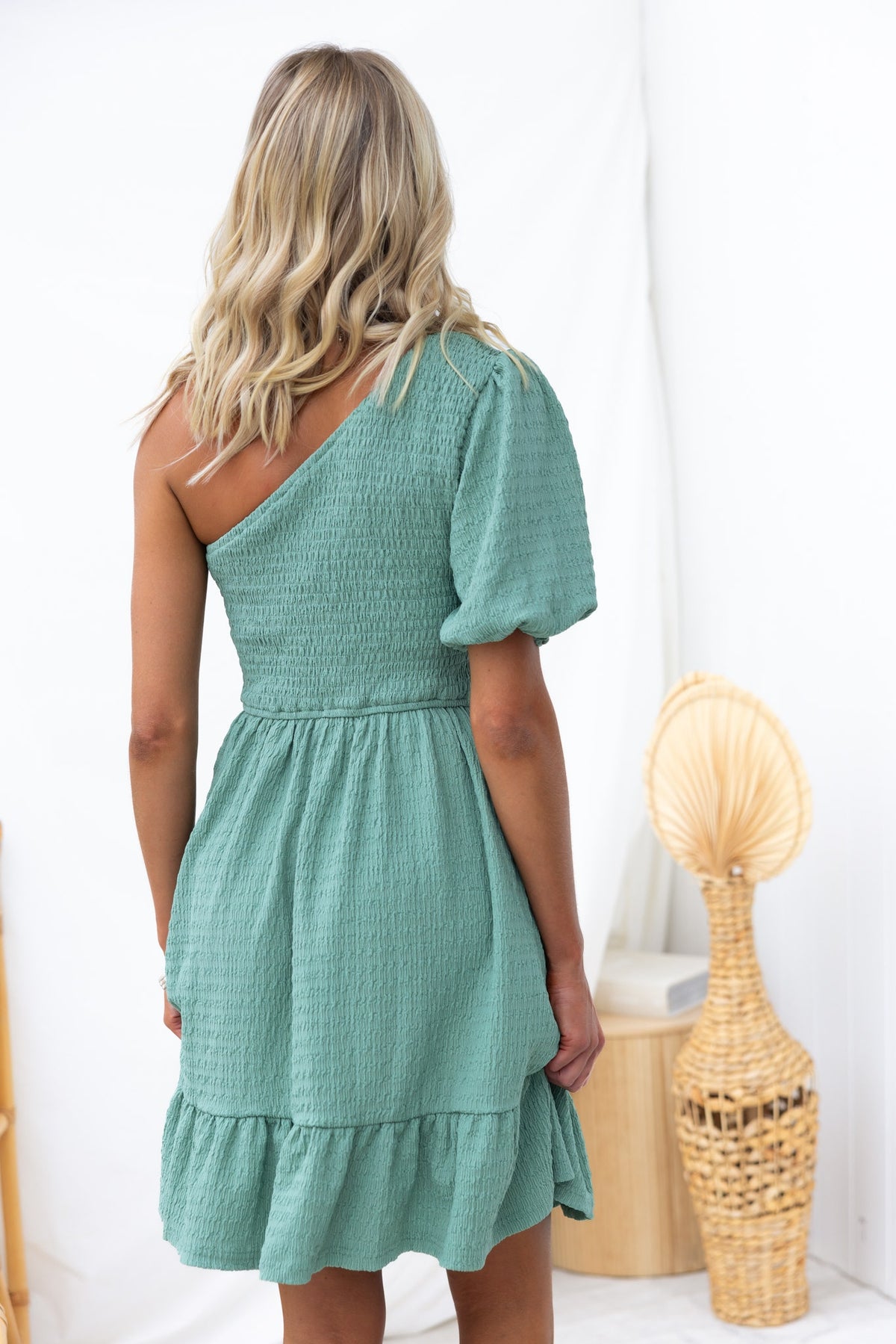Woman wearing a green Galvez dress with a one-shoulder neckline and textured fabric, showcasing a relaxed fit and ruffle hem.