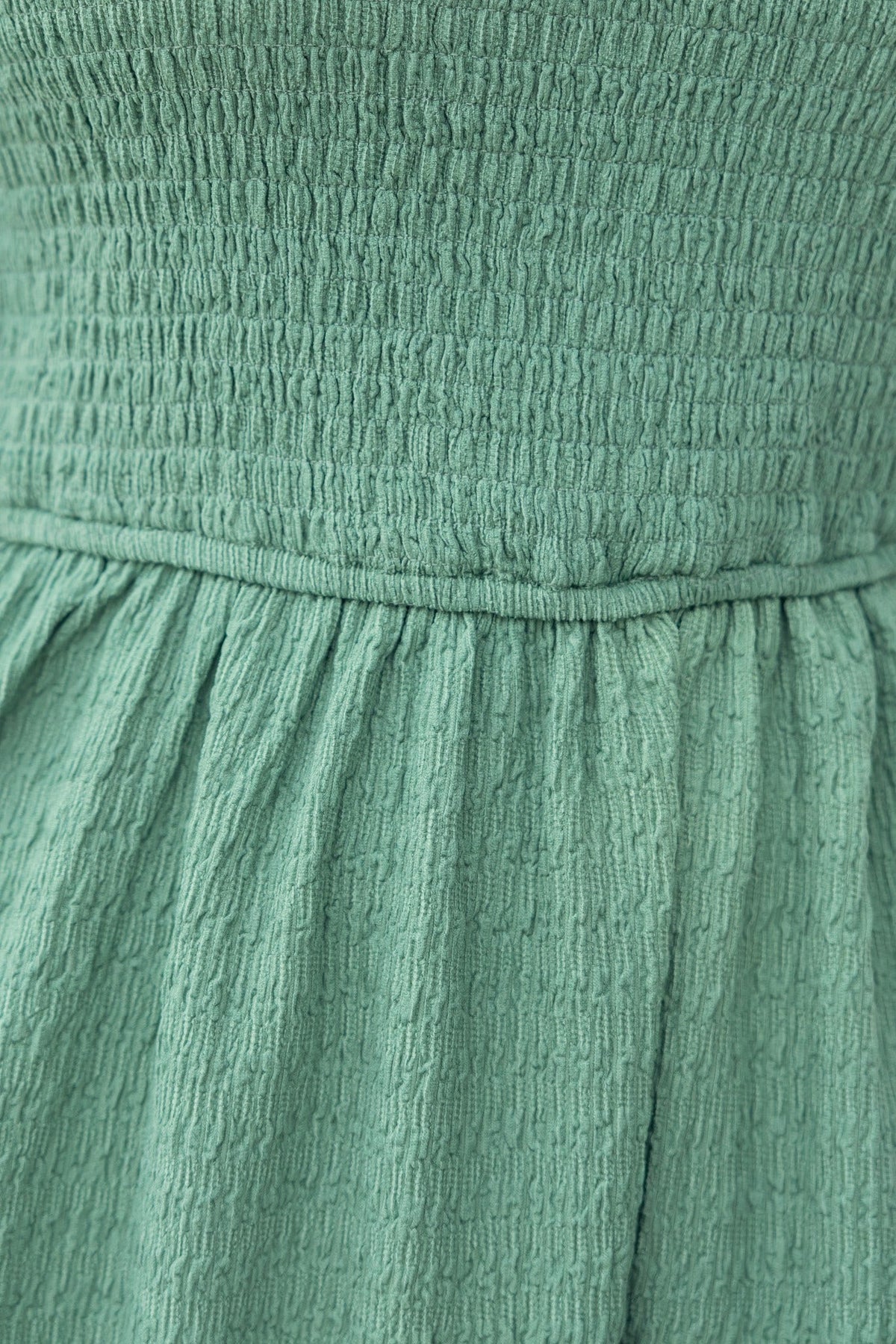 Close-up of the textured green fabric of the Galvez Dress featuring a smocked bodice and gathered skirt.