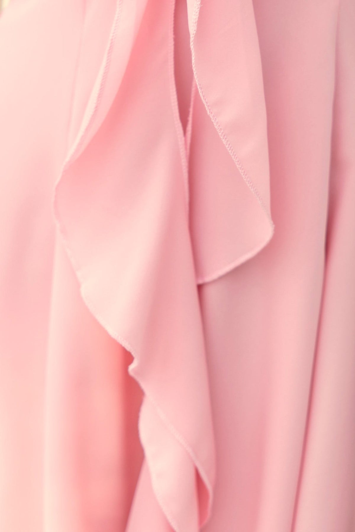 Close-up of soft pink chiffon fabric with flowing ruffles, highlighting texture and elegance for fashion items.