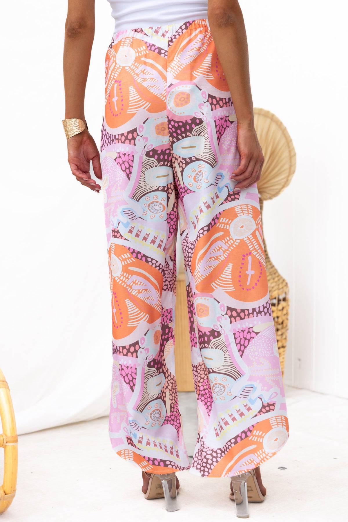 Back view of model wearing Kamilla pants with abstract print in vibrant colors, showcasing wrap tie and mid-high waist fit.