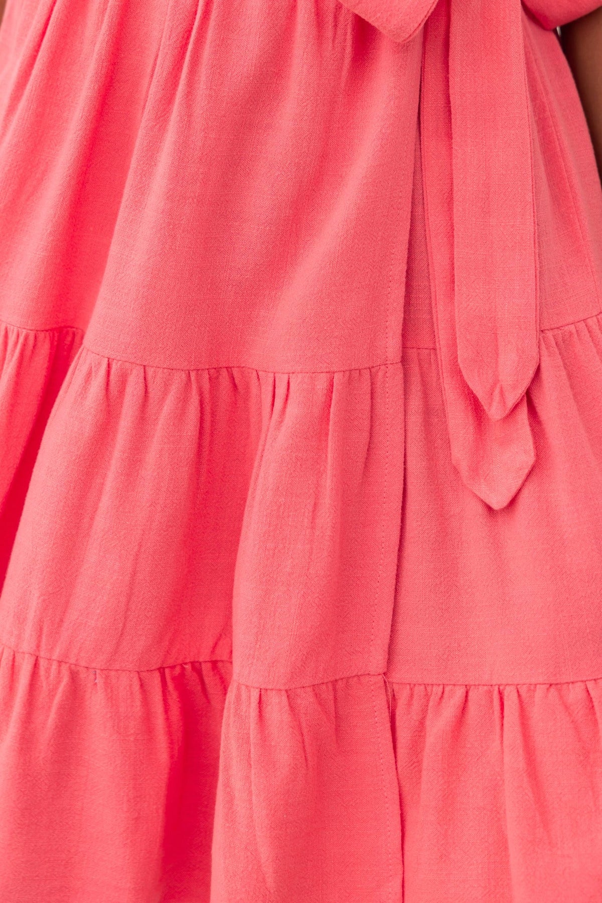 Close-up of the cerise wrap dress showcasing the fabric tie and tiered design.
