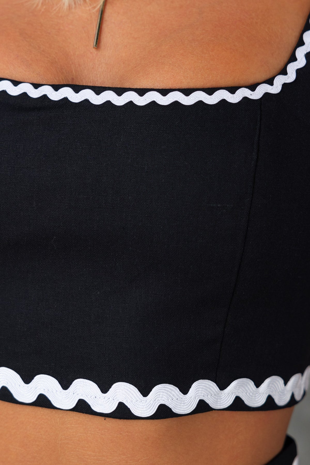 Close-up of Harriette Top's black fabric with square neckline and white scalloped trim.
