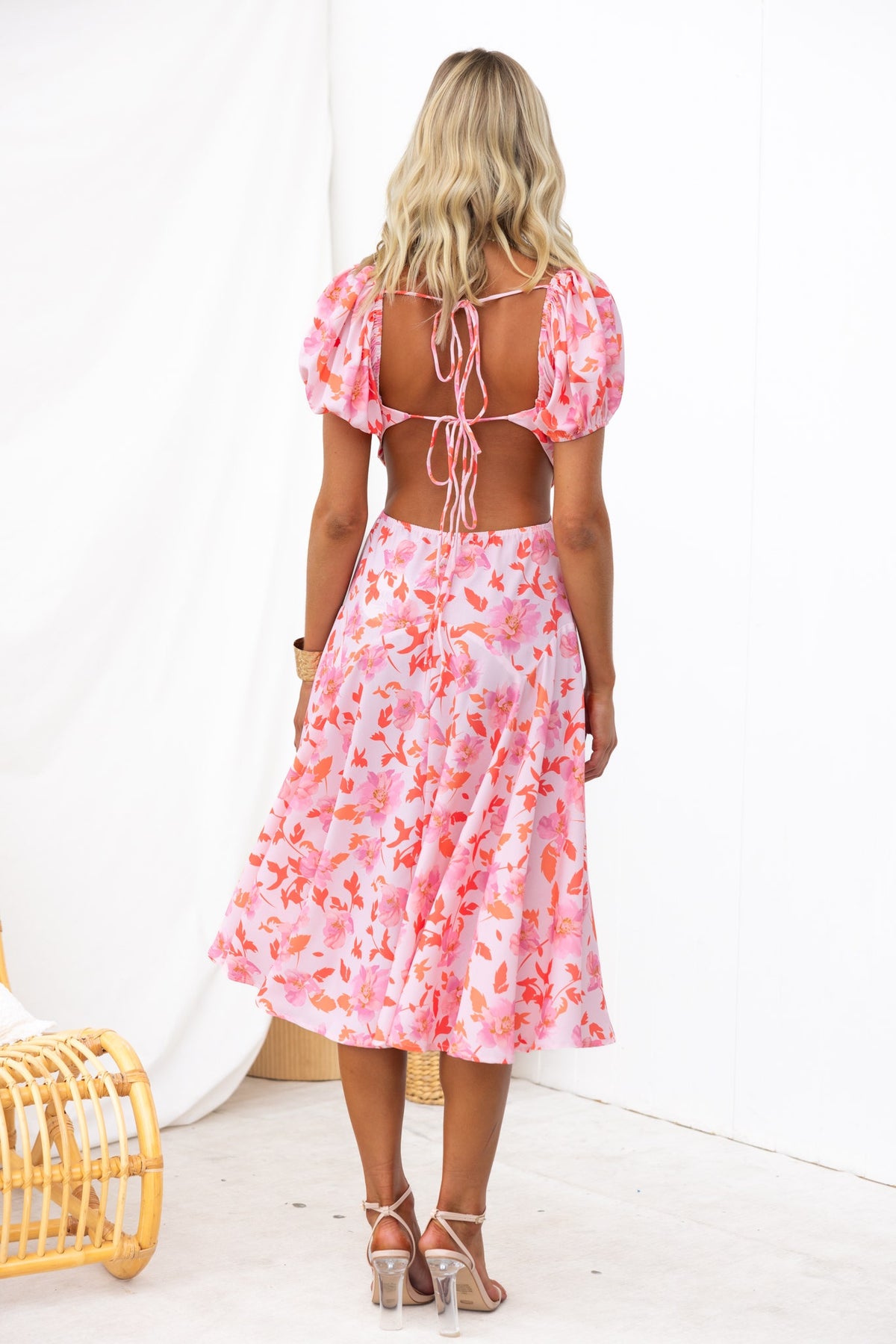 Back view of a woman in a floral print pink midi dress with puff sleeves and a tie-back detail.