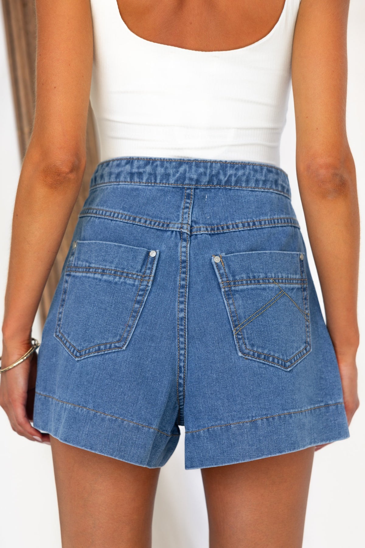 Back view of Colden denim shorts with high waist fit and pockets, styled with a white tank top.