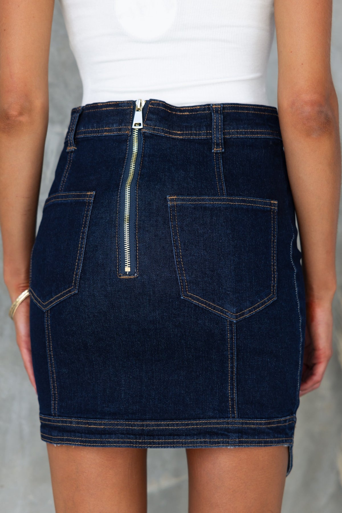 Back view of Anni Denim Skirt featuring a zip closure, pockets, and lightly frayed hemline in dark navy denim.