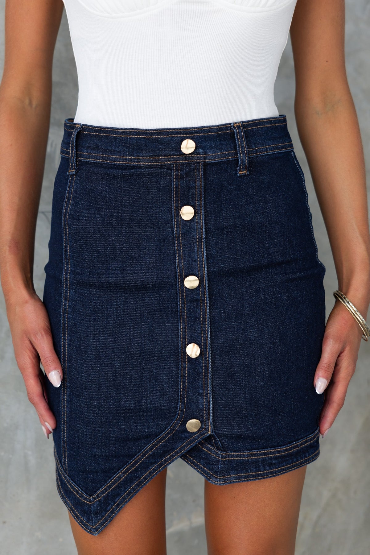 Dark navy denim skirt with faux buttons, mid-high waist, and lightly frayed hemline, perfect for casual outfits.