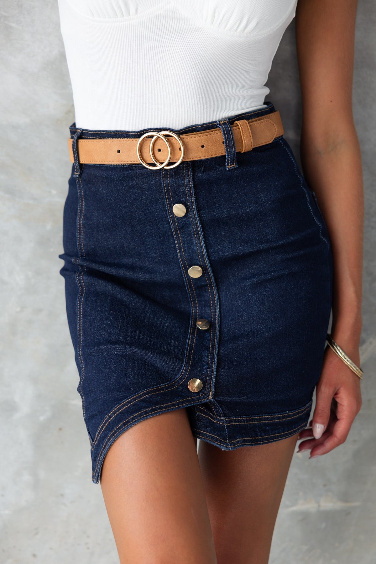Fashionable dark navy denim skirt with faux buttons and a mid-high waist fit, styled with a tan belt.