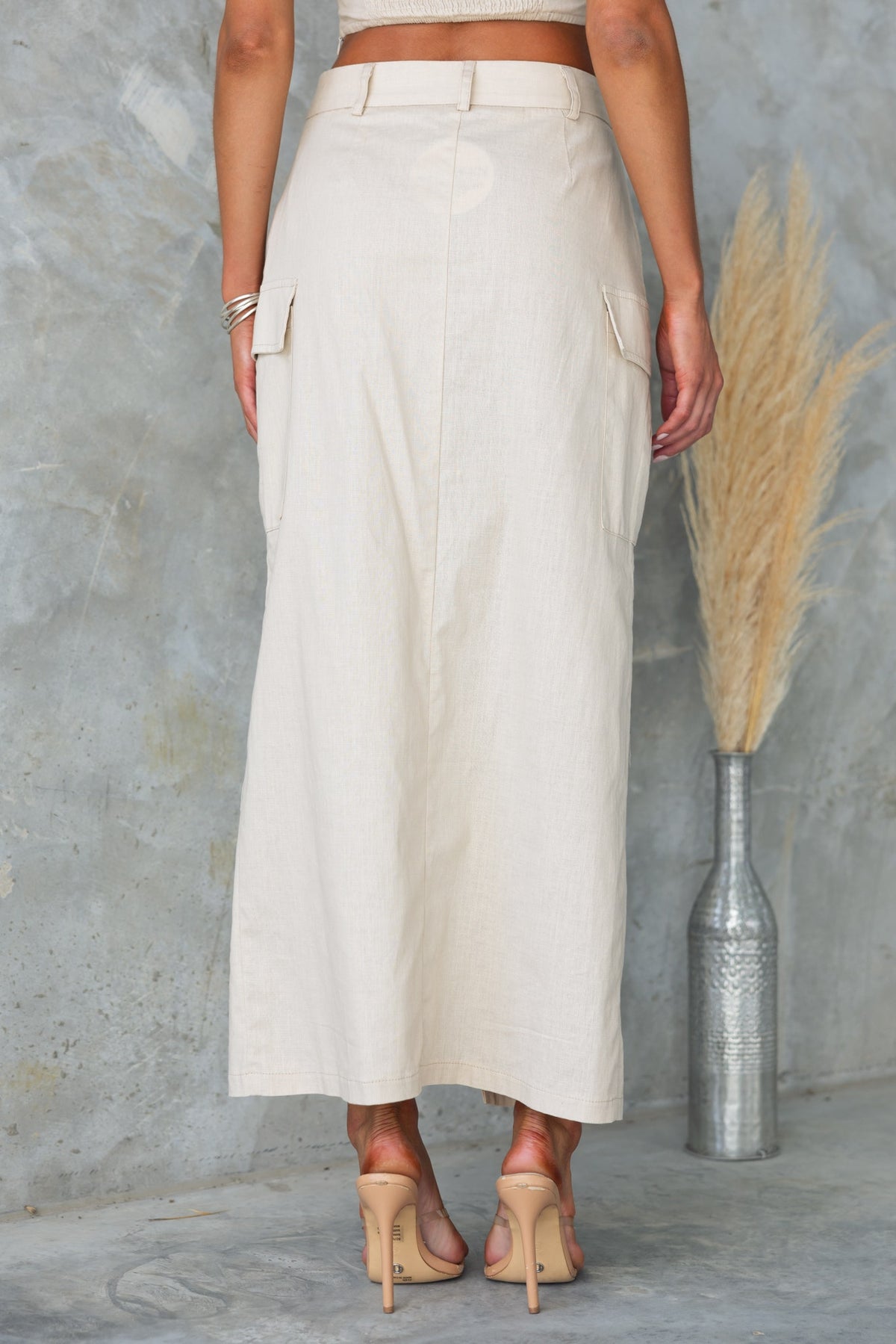 Back view of Lyra Maxi Skirt featuring pockets, mid-waist fit, and a light cotton feel, styled with high heels.