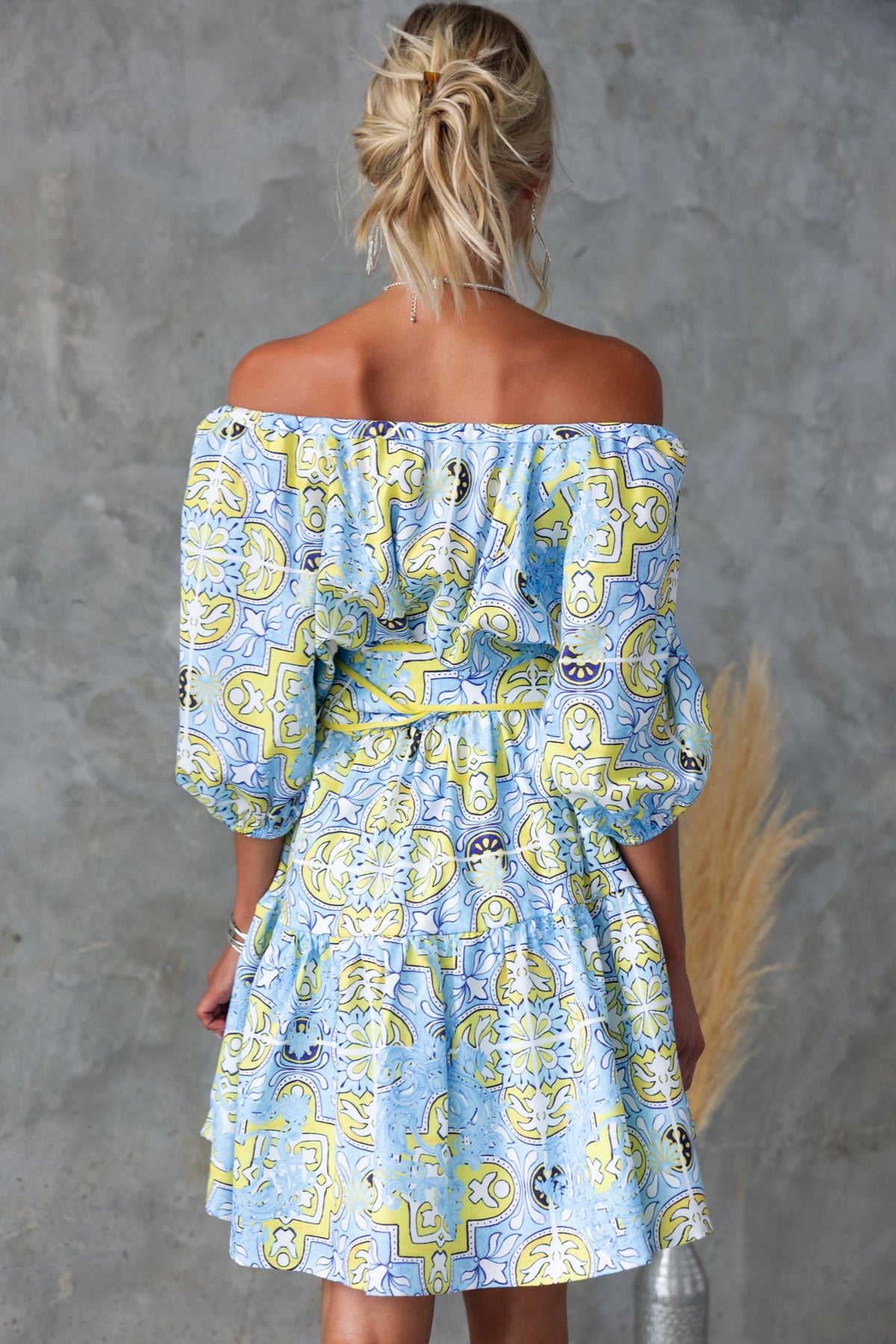 Back view of a colorful abstract print off-shoulder dress with a fabric belt and puff sleeves.