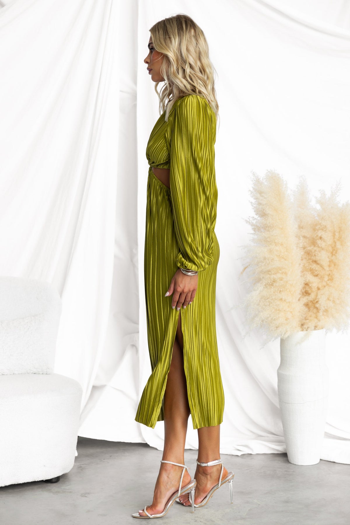 Aulia Midi Dress in olive green with accordion pleats, V-neckline, and side split, modeled elegantly against a white backdrop.