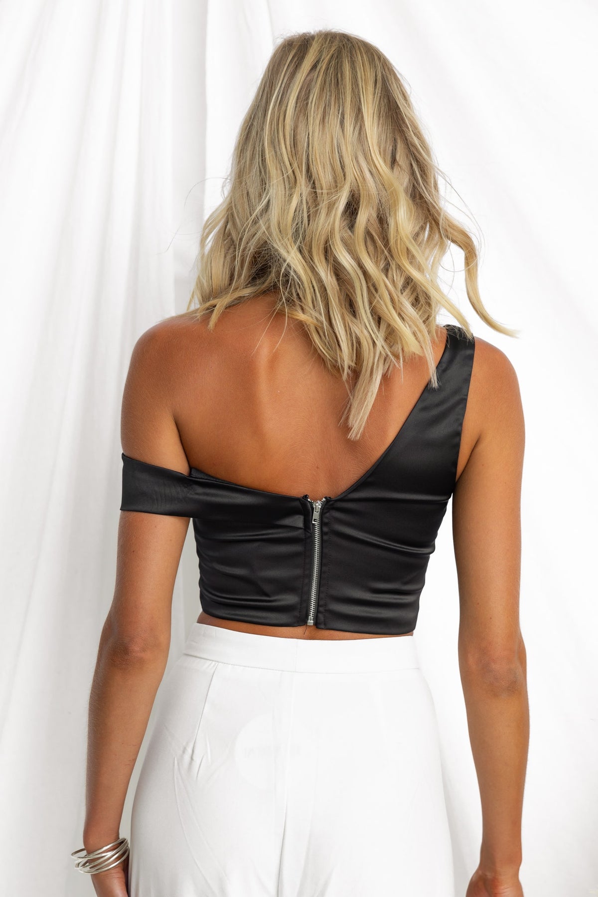 Back view of Zoya Top in black satin with an asymmetric neckline and zip closure.