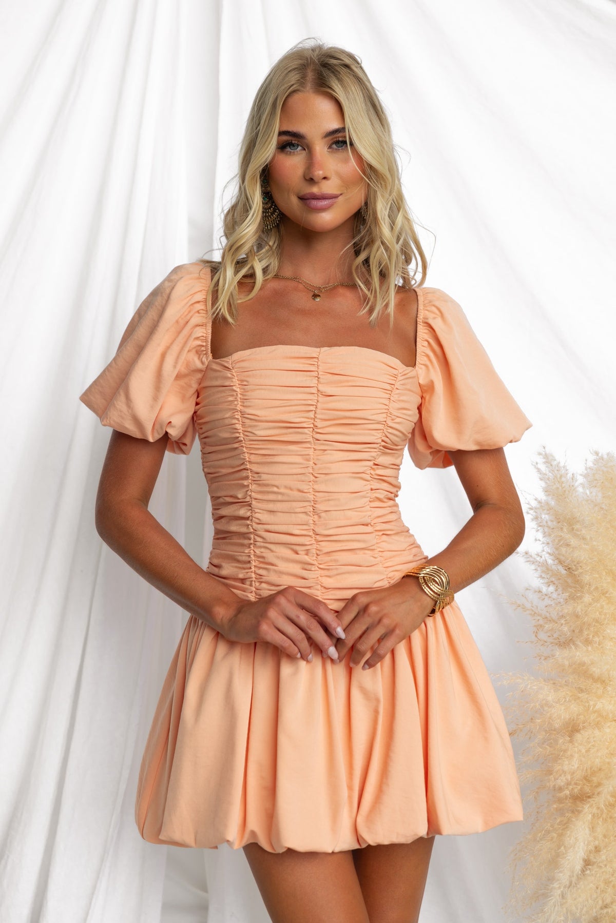 Model wearing the Margie Dress, featuring a square neckline, puff sleeves, and a flattering ruched bodice in peach color.