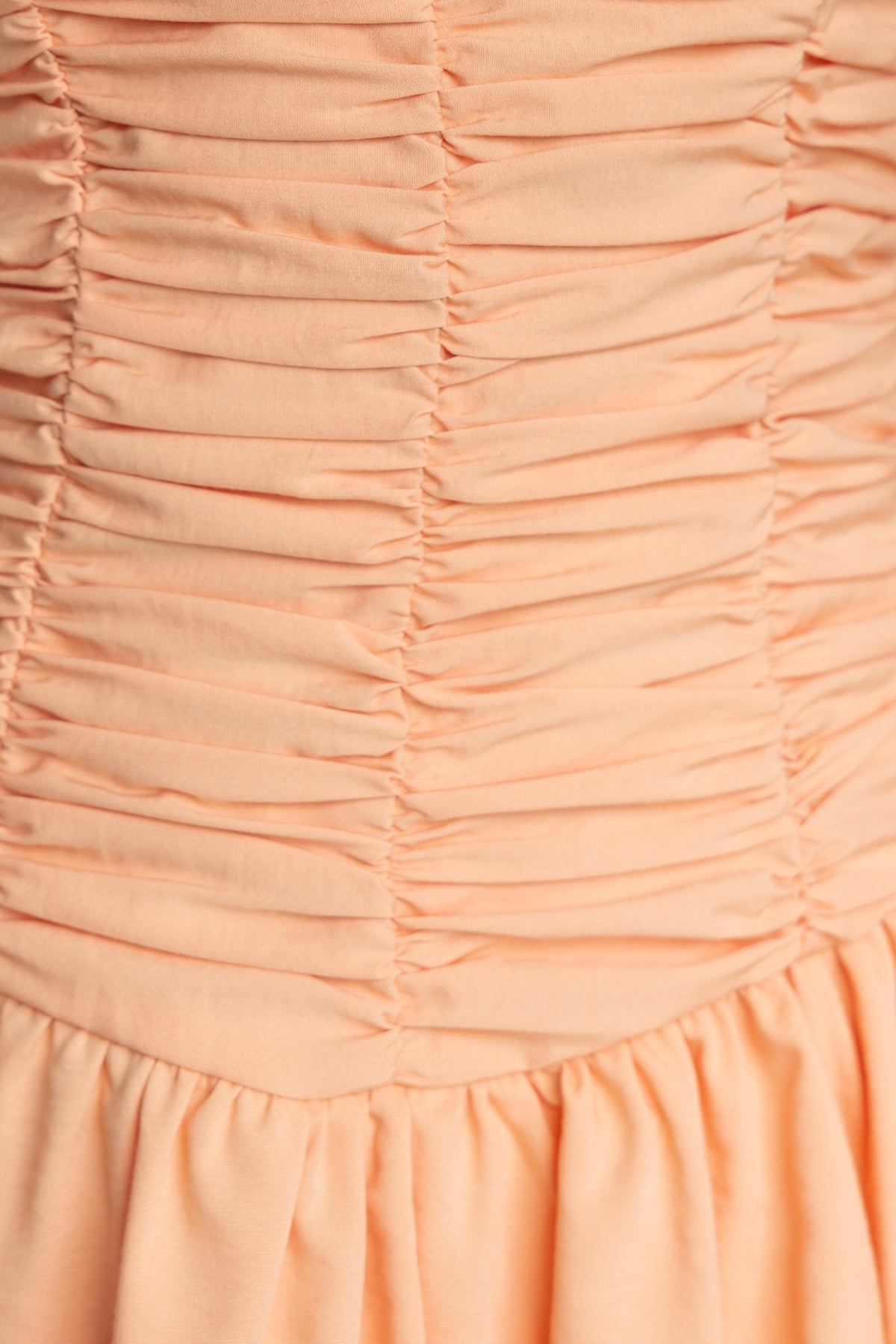 Close-up of the pleated detail on the Margie Dress in soft peach color, showcasing the square neckline and gathering.