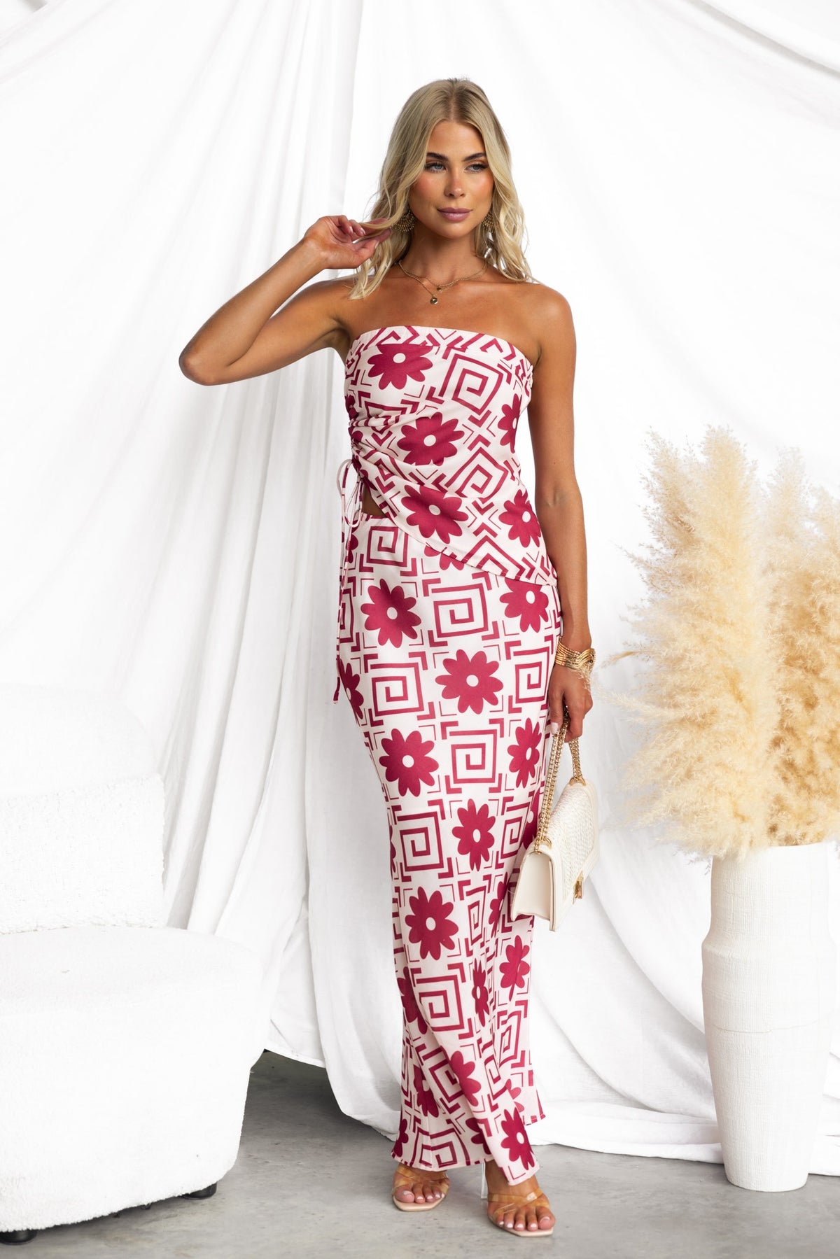 Model wearing floral maxi dress with geometric patterns, featuring a strapless design and fitted silhouette.