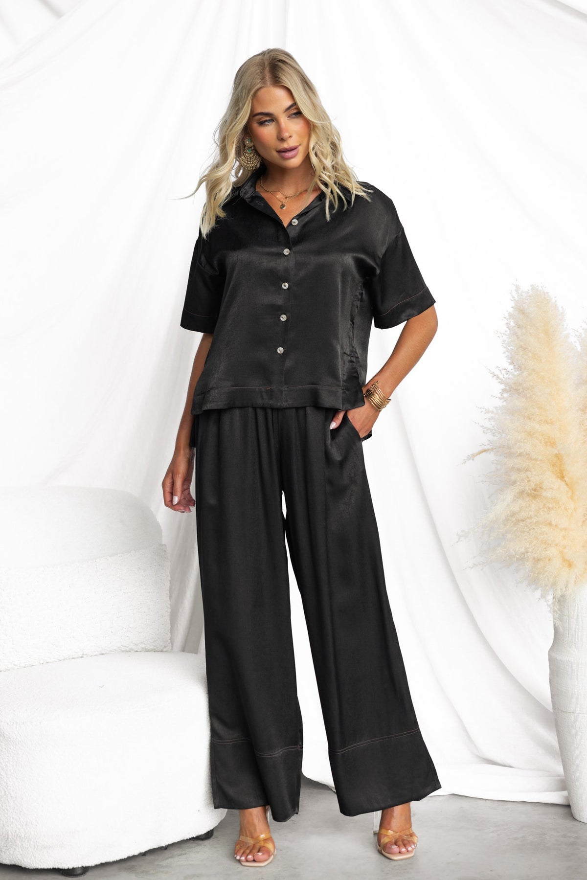 Model wearing black Noel Pants with mid-high waist fit and a silky feel, styled with a matching black top.