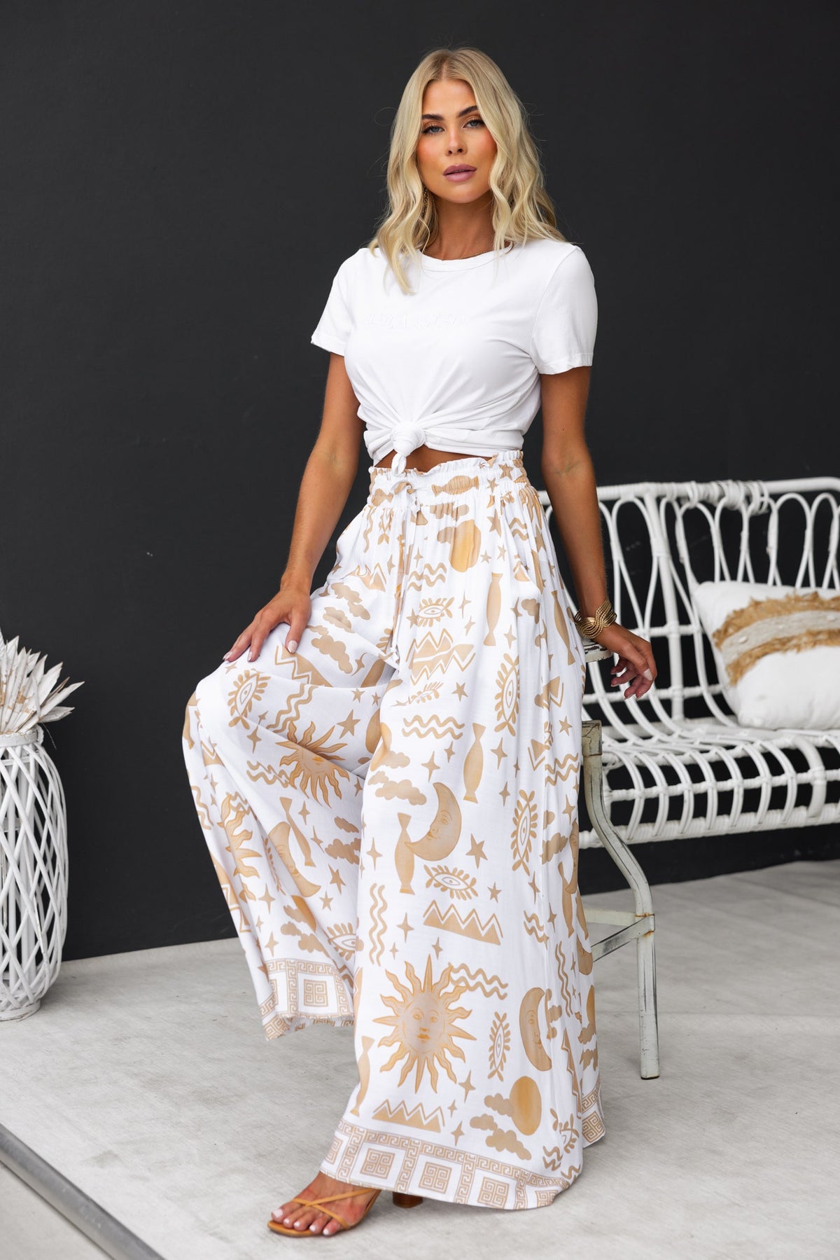 Model wearing Amadi abstract print pants with wide legs and a white crop top, styled in a chic setting.