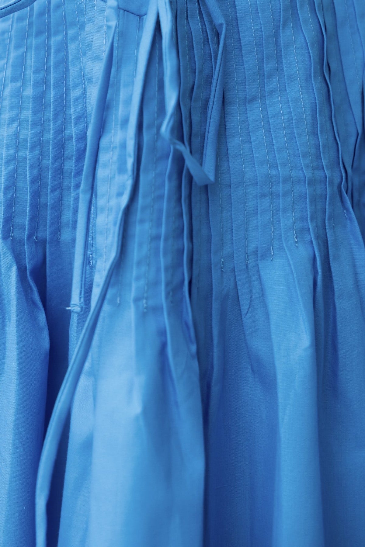 Close-up of a pleated blue dress featuring off-shoulder design and tie detail.